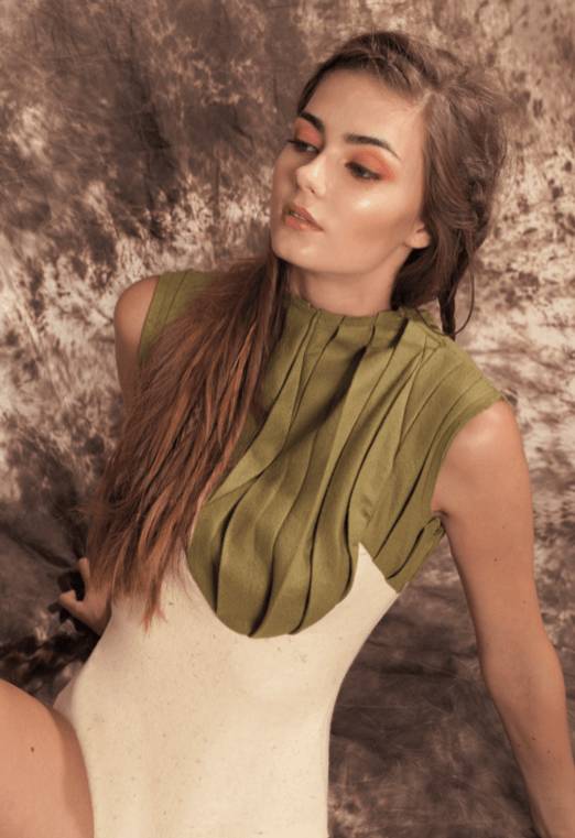 Una modelo posa con un vestido elegante de colores neutros y un top verde con pliegues.