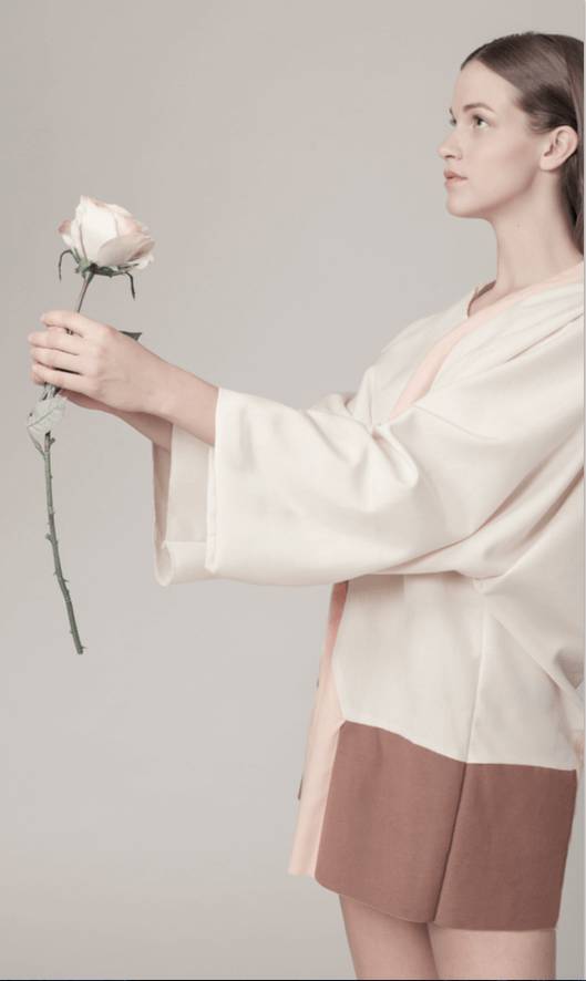 Una mujer sostiene una rosa mientras viste una prenda de diseño minimalista.