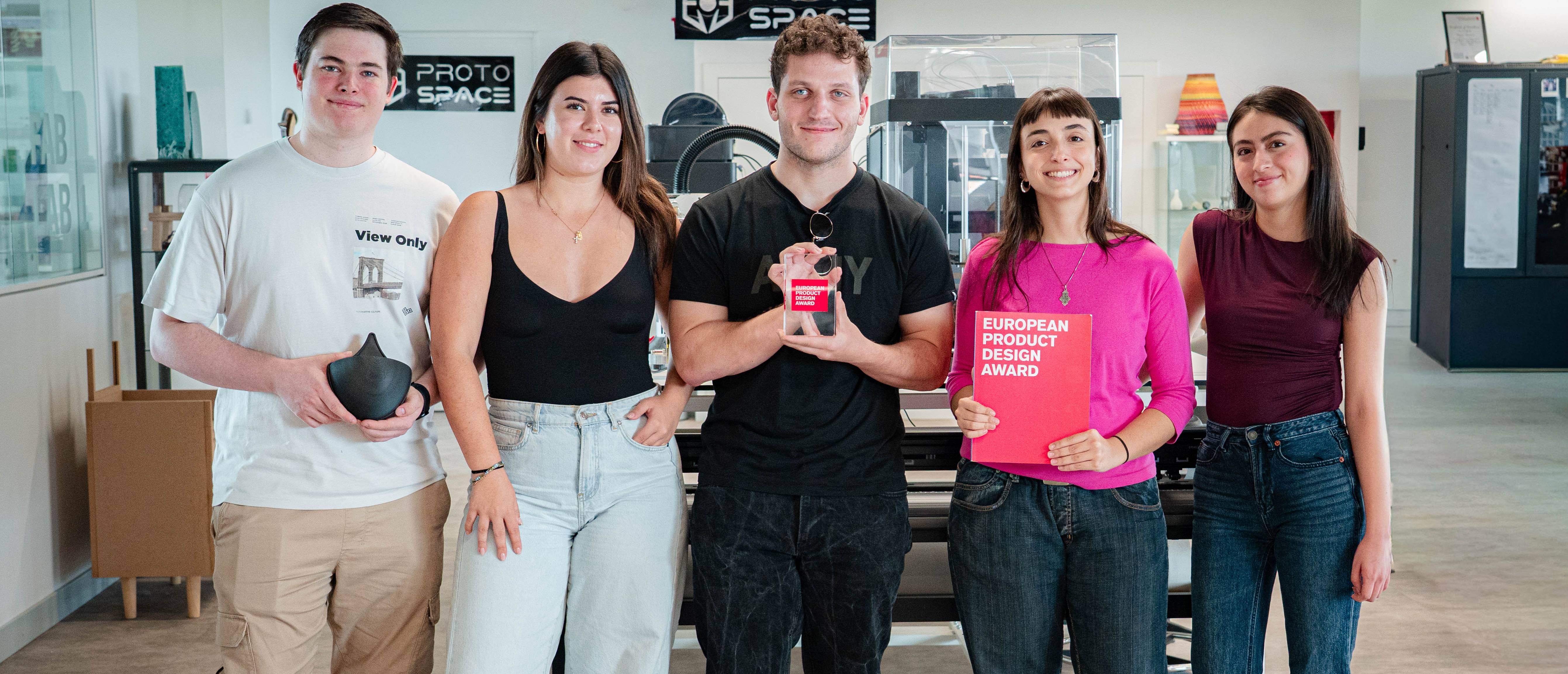 Un grupo de cinco personas sonríen mientras sostienen premios y reconocimientos en un entorno de trabajo moderno.