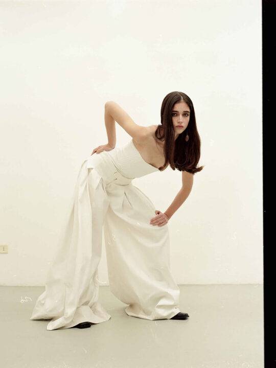 Una modelo posando con un conjunto blanco y un fondo neutro.