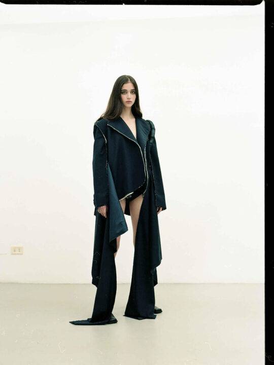 Una modelo posa en un espacio minimalista con un atuendo de diseño moderno y asimétrico.