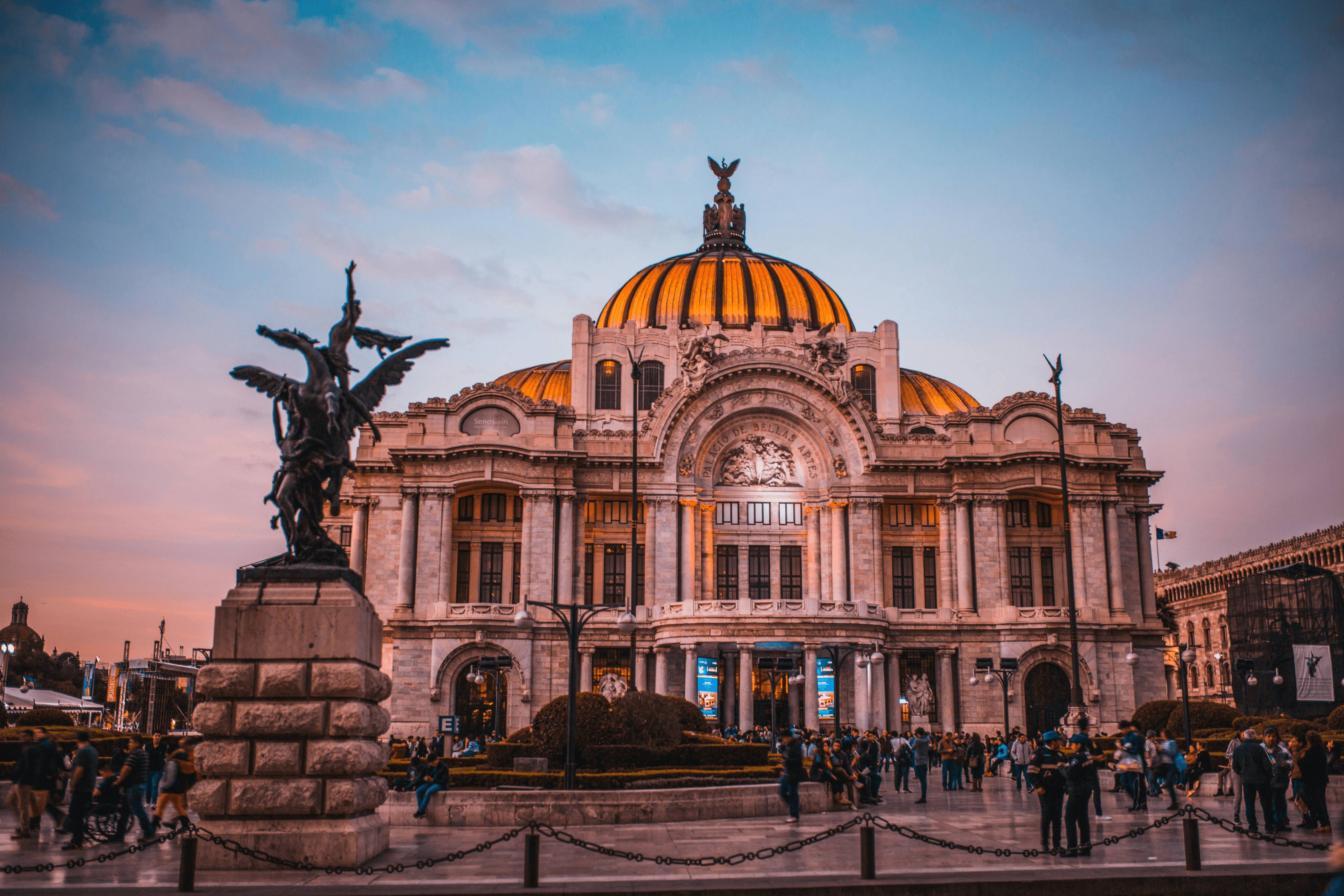 Edificio monumental con cúpula de color amarillo y una estatua en primer plano durante el atardecer.