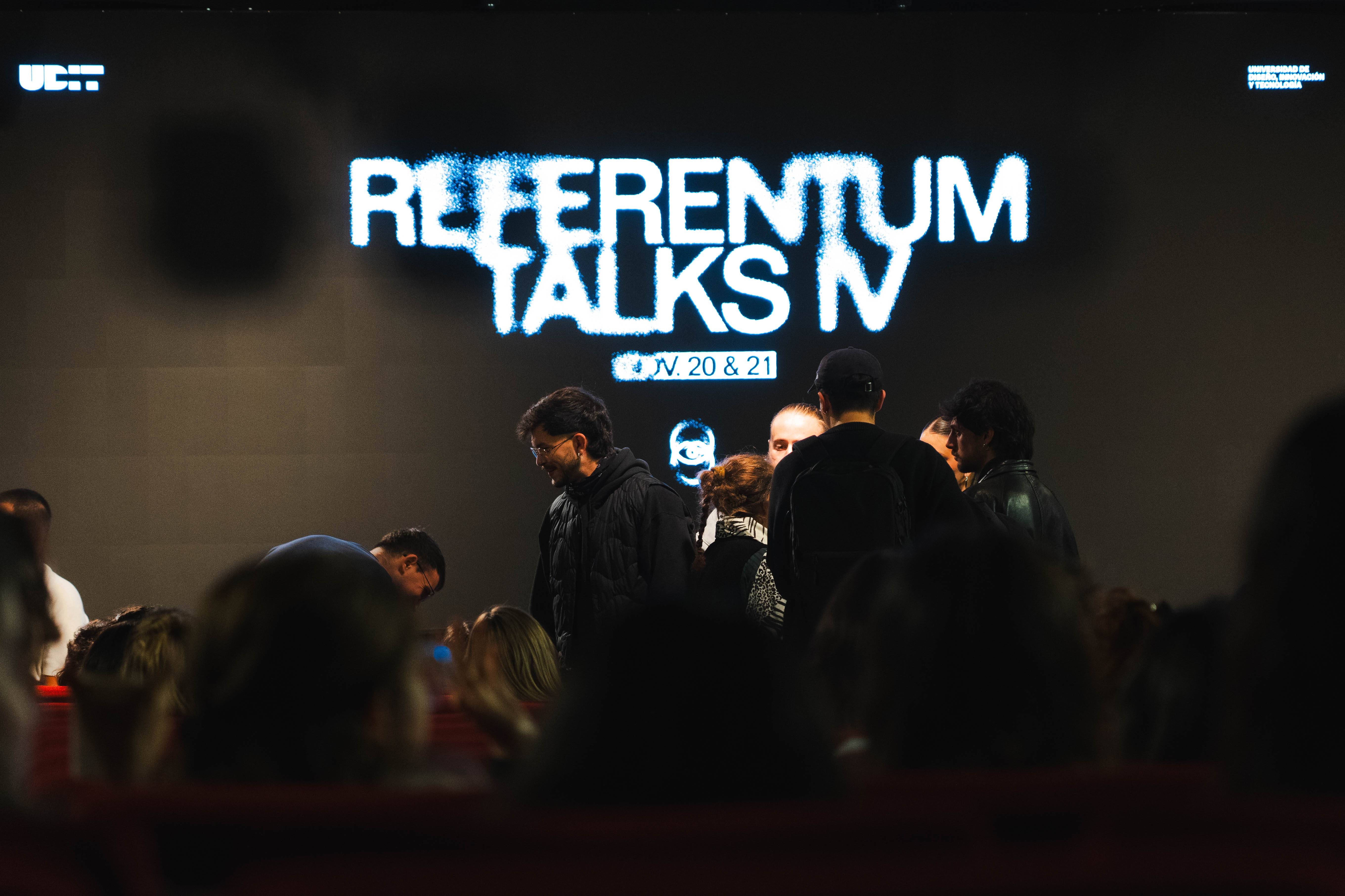 Una multitud se agrupa frente a una pantalla que anuncia el evento Referentum Talks IV.