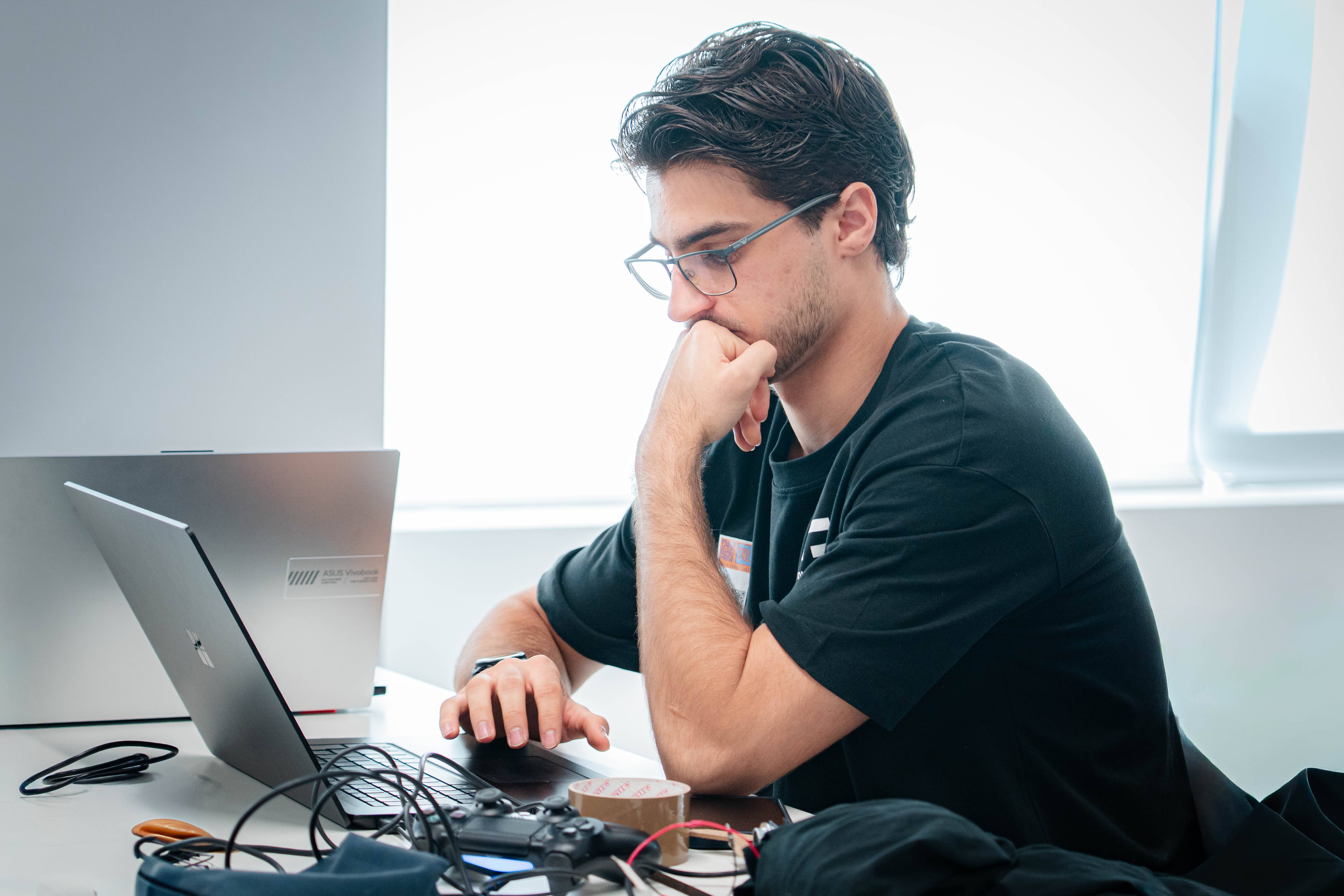 Un joven concentrado trabajando en una computadora portátil en una mesa.
