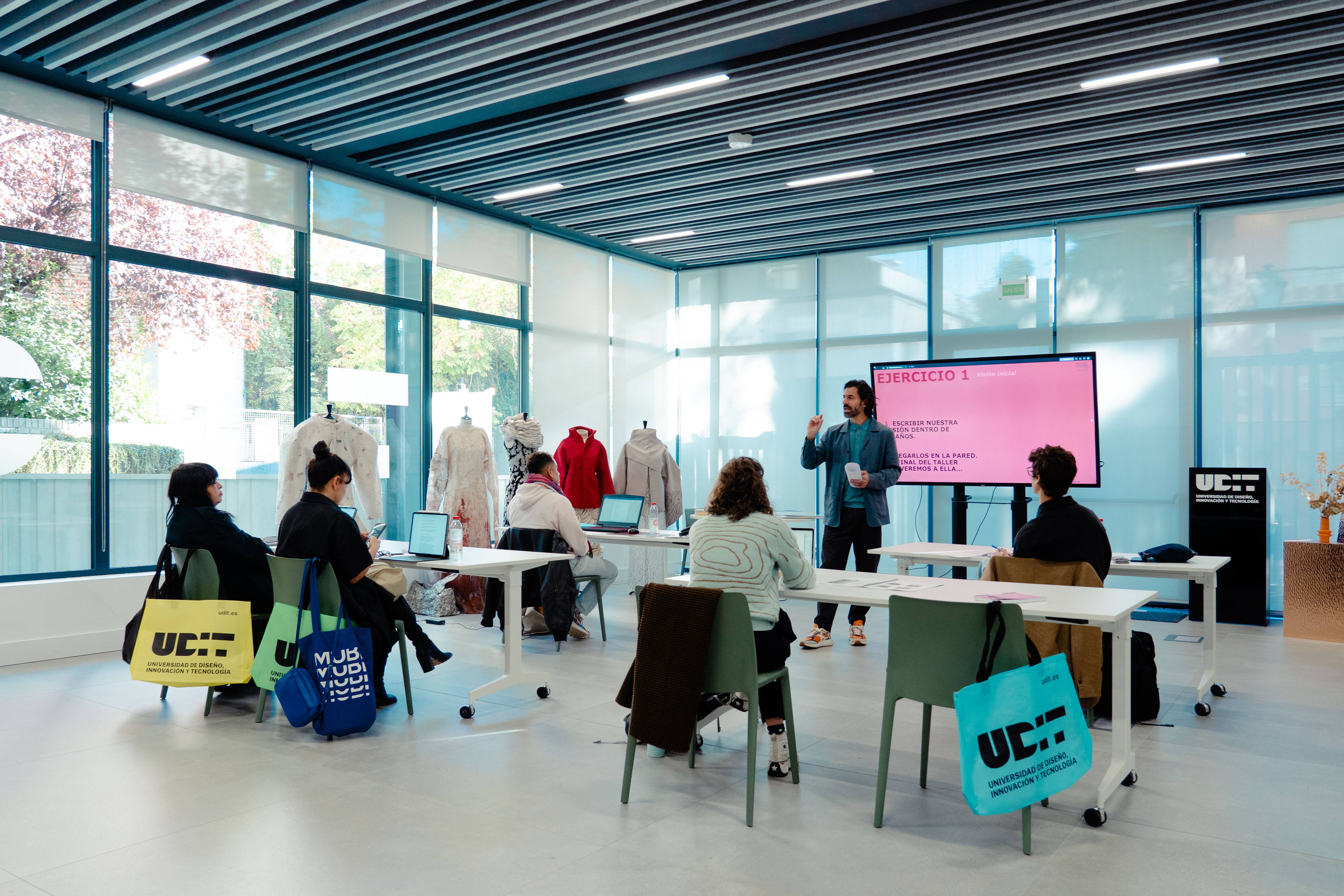 Un grupo de personas asiste a una clase en un aula moderna con pantallas y ordenadores.