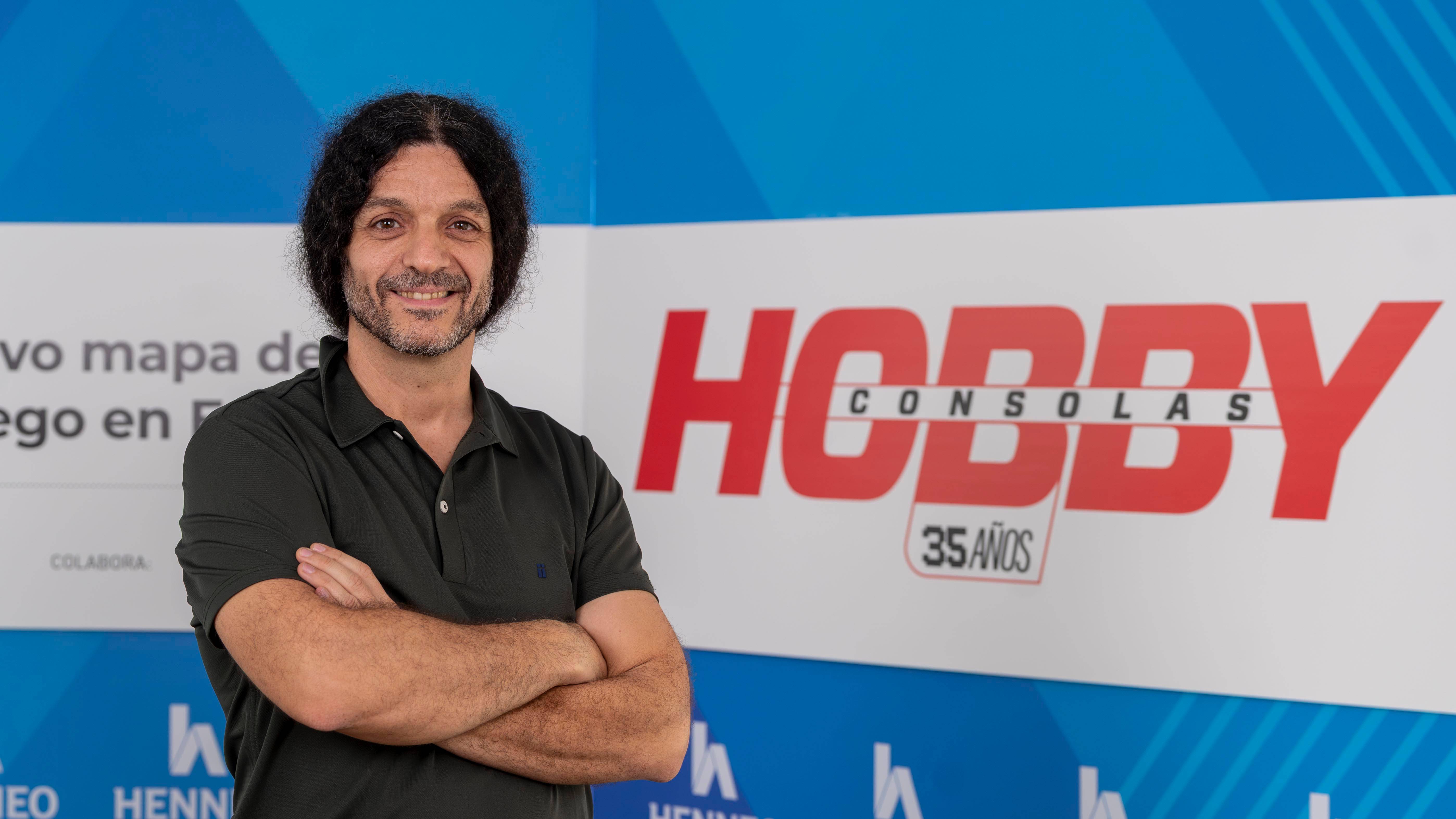 Una persona sonriente posa frente a un fondo que celebra el 35 aniversario de Hobby Consolas.