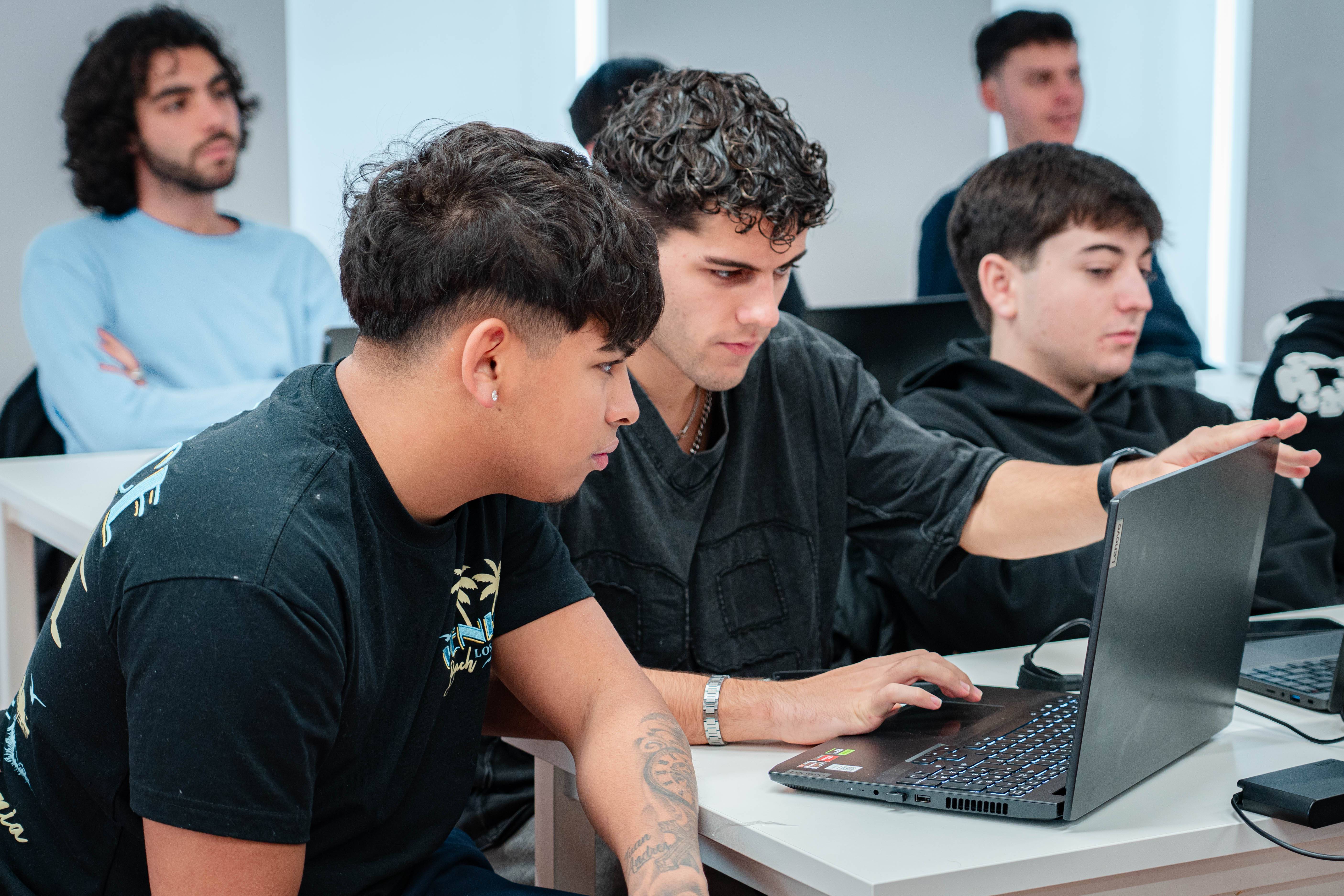 Un grupo de jóvenes se encuentra en un aula, algunos observando una computadora portátil.
