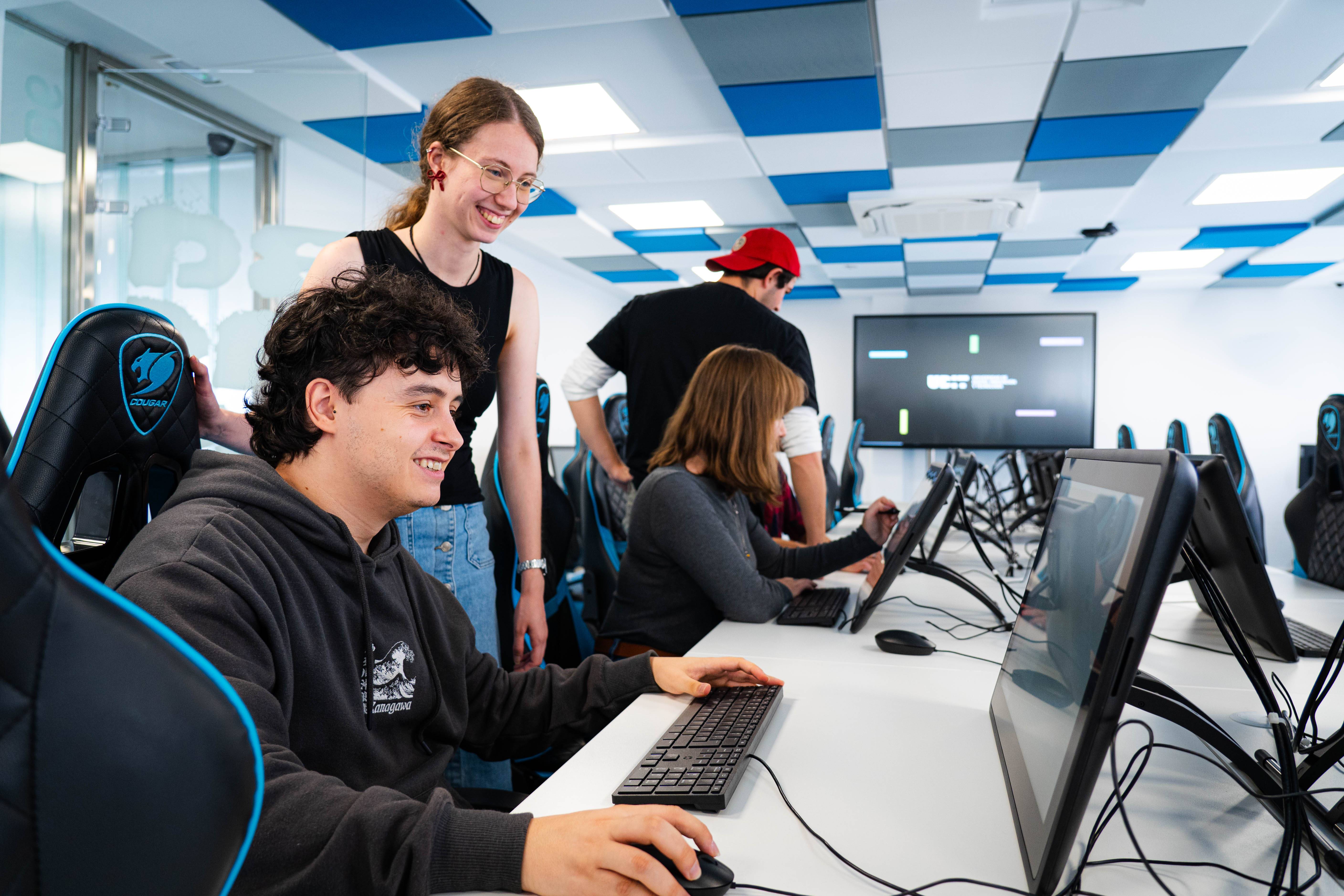 Un grupo de jóvenes se encuentra en un aula de computación, sonriendo y trabajando en las computadoras.