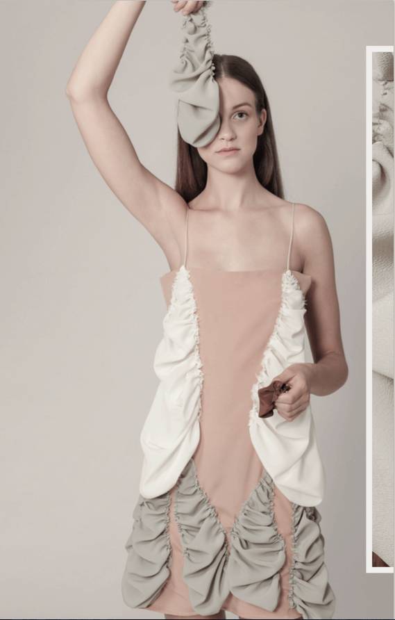 Una modelo sostiene una prenda con pliegues en tonos suaves, mostrando un estilo moderno y artístico.