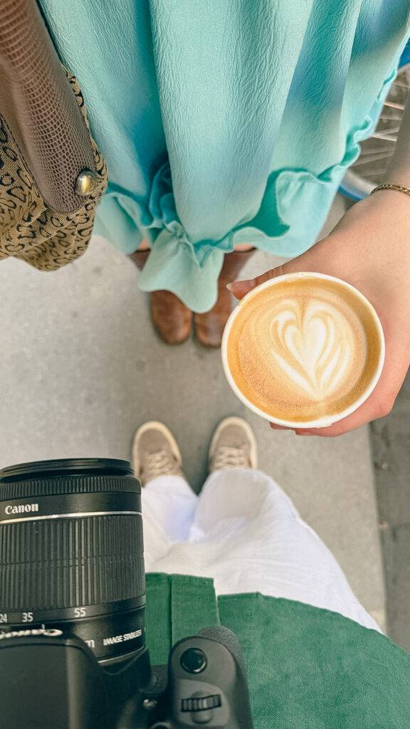 Una persona sostiene un café con arte latte mientras otra persona está de pie a su lado, ambas con un fondo urbano.