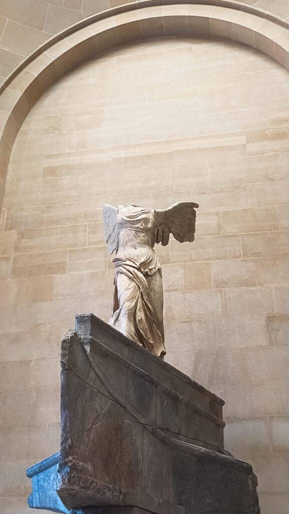 La imagen muestra la famosa escultura de la Victoria de Samotracia, que representa a una figura alada en un pedestal.