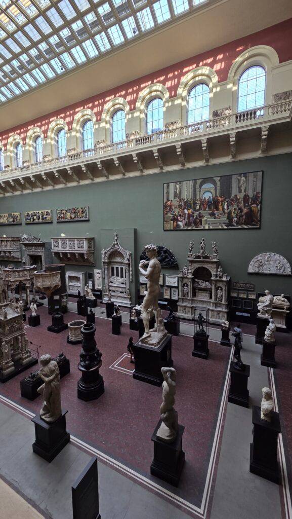 La imagen muestra una gran sala de museo con esculturas y una pintura al fondo.