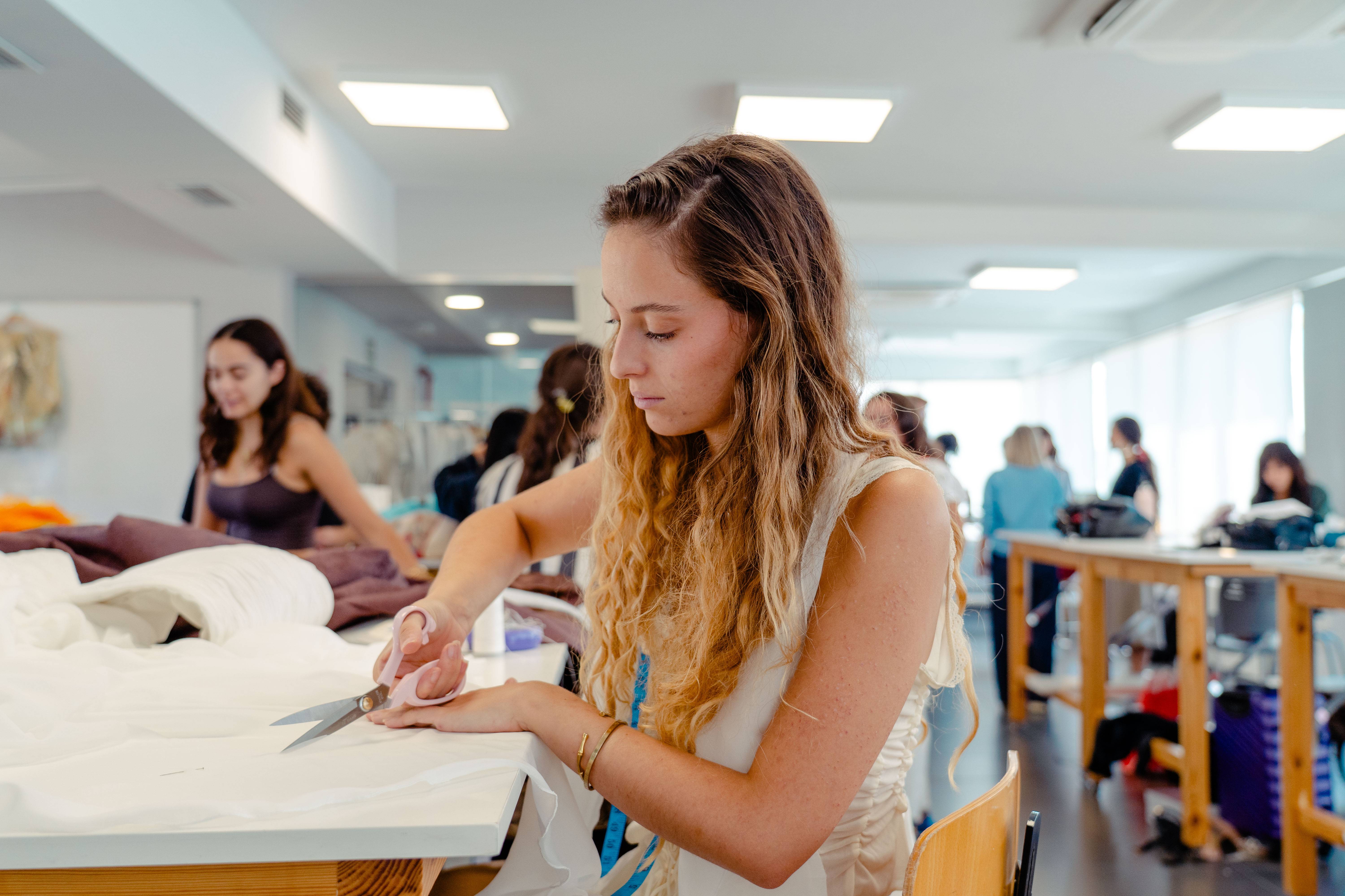 Una mujer joven está cortando tela en un entorno de clase de costura.