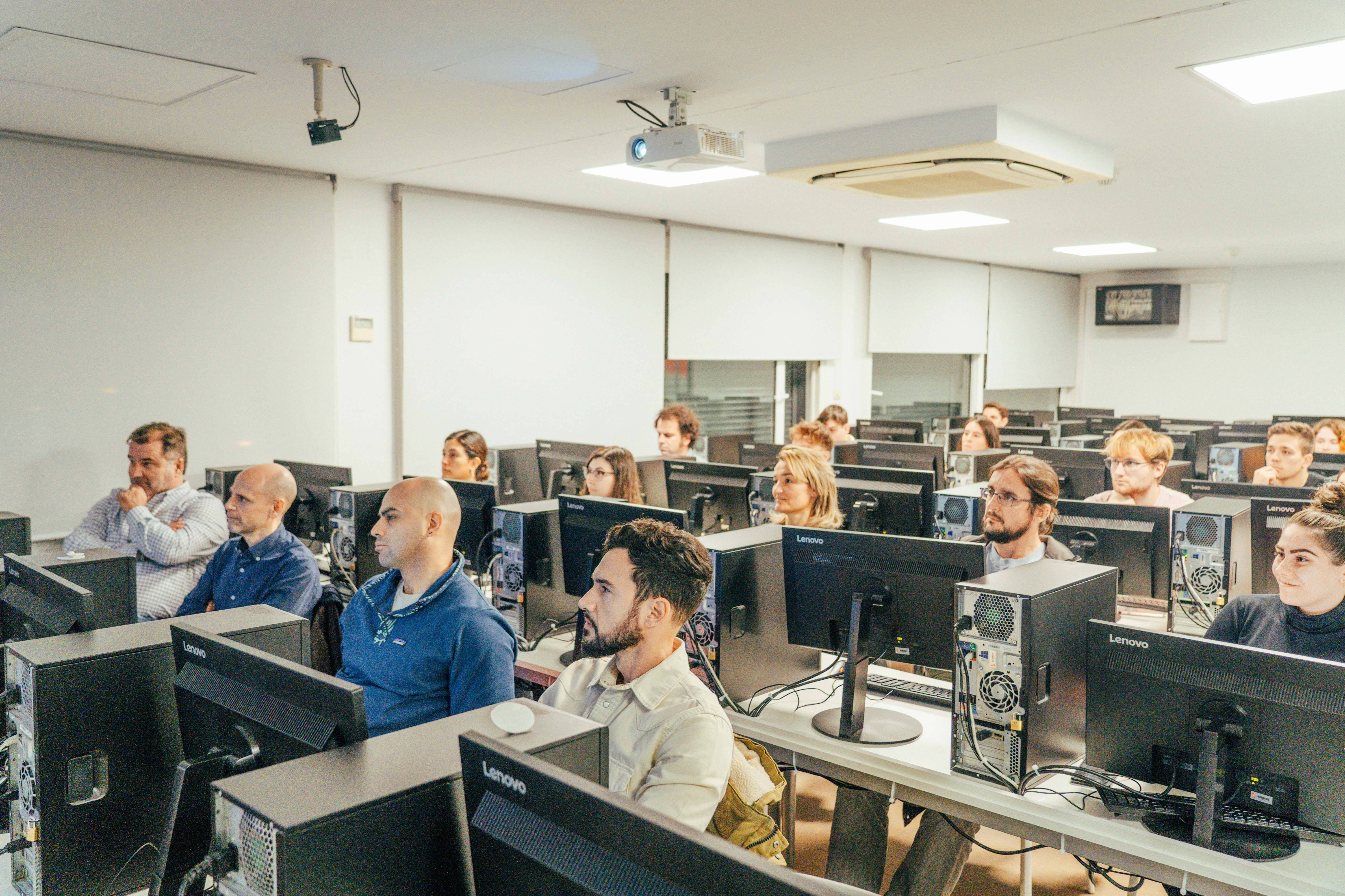 Un grupo de personas asistiendo a una clase en un aula con computadoras.