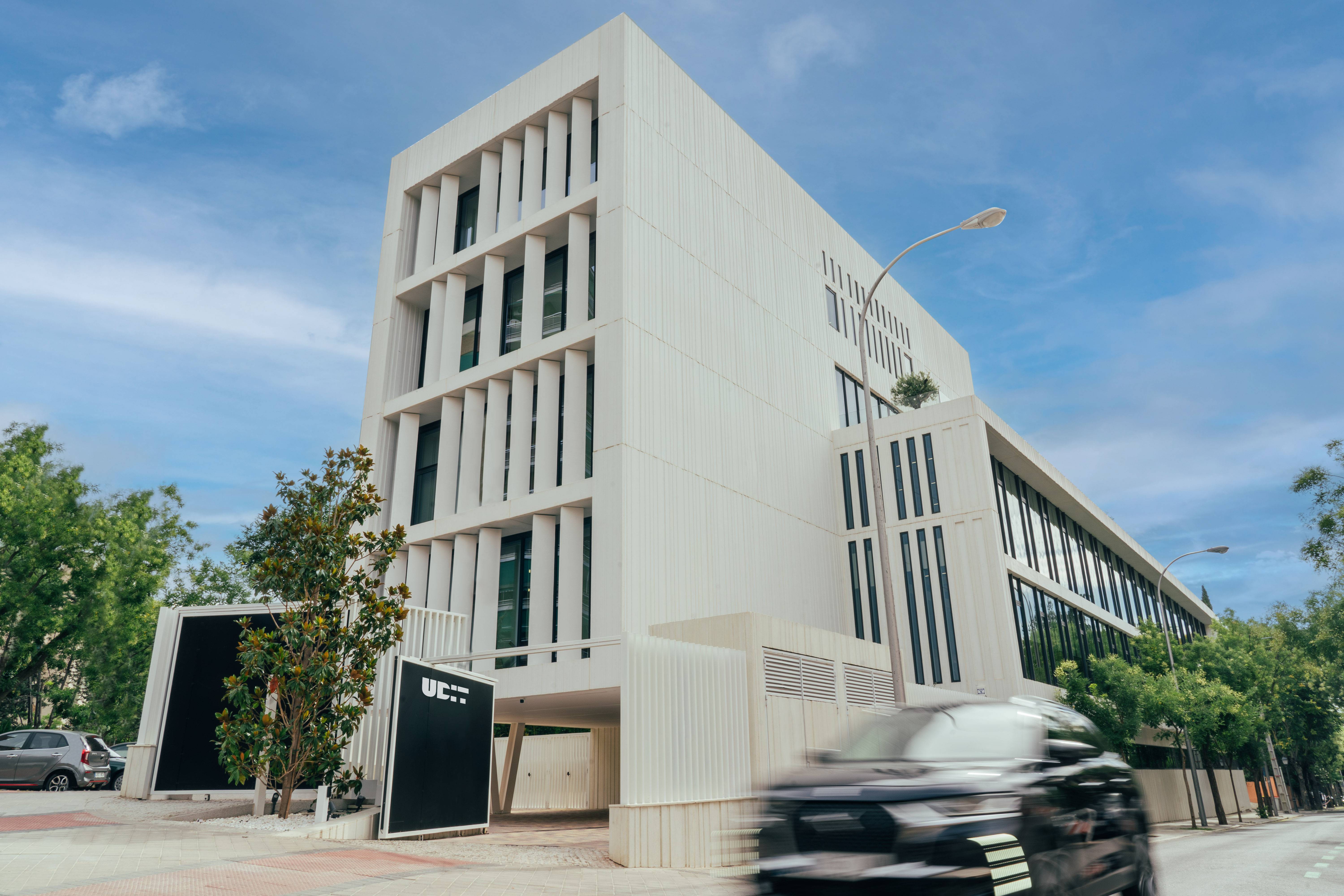 Edificio moderno con fachada blanca y vegetación alrededor.
