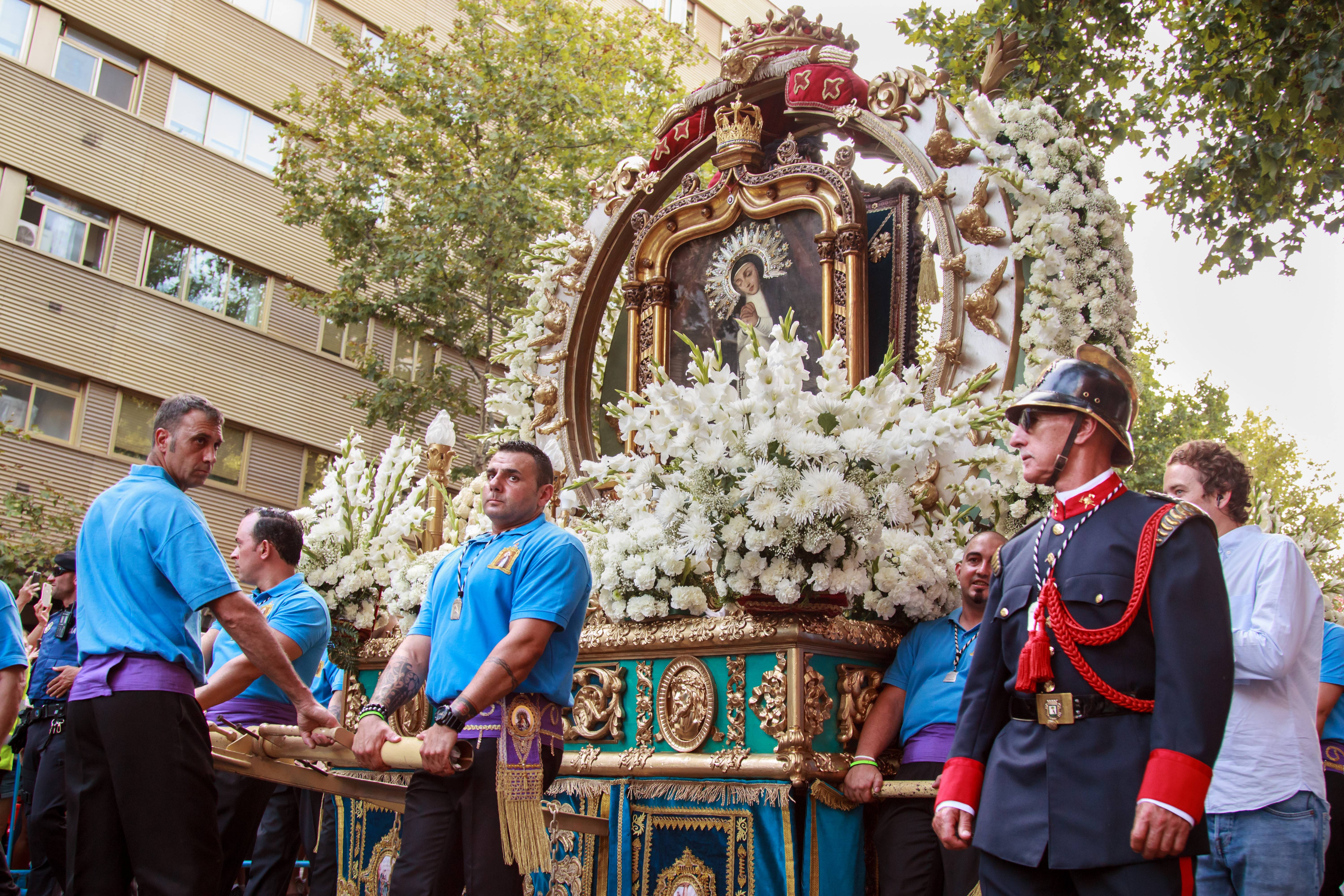 Desfile de una procesión con un paso religioso ornamentado lleno de flores.