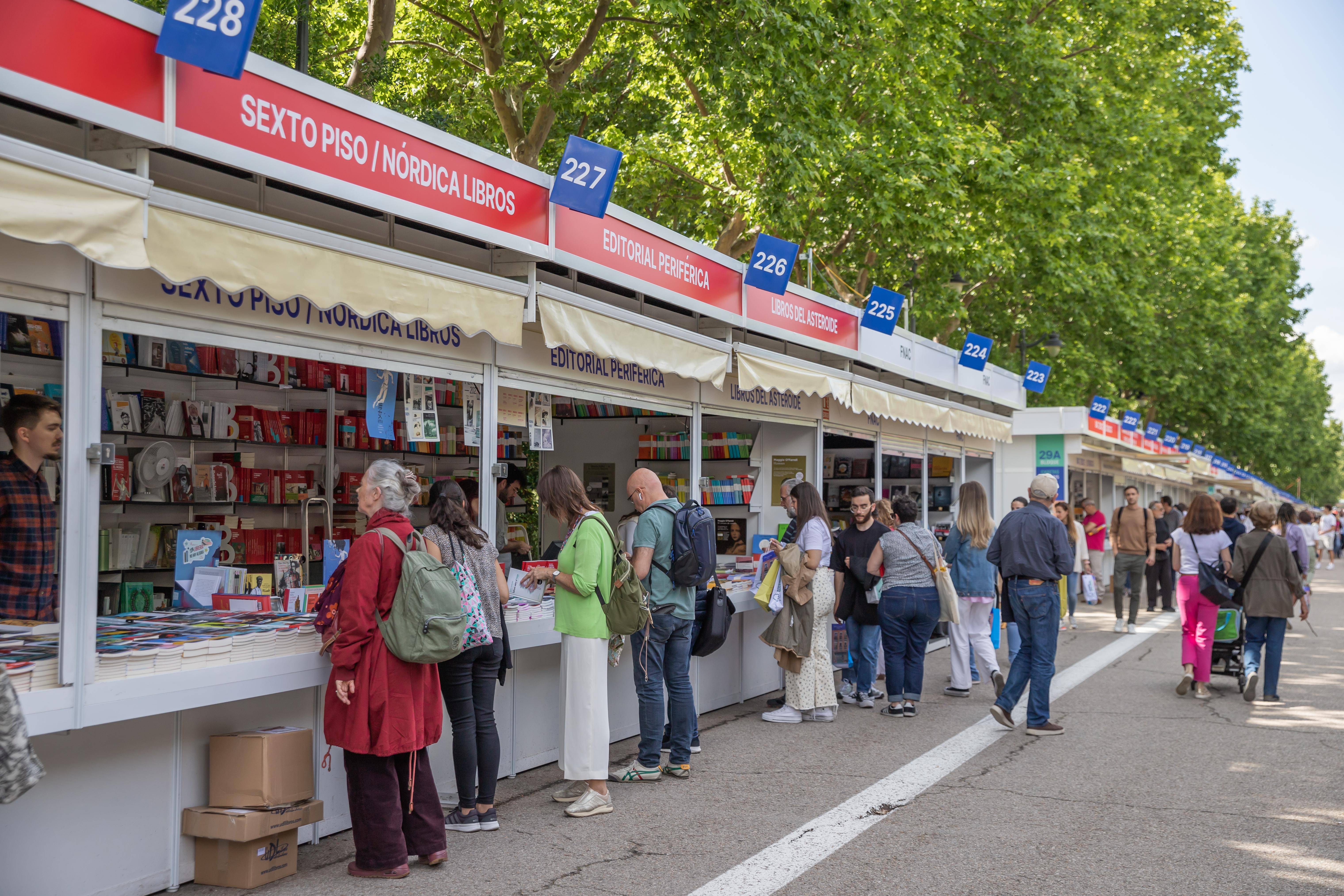 Una feria del libro al aire libre con varios puestos y asistentes mirando libros.