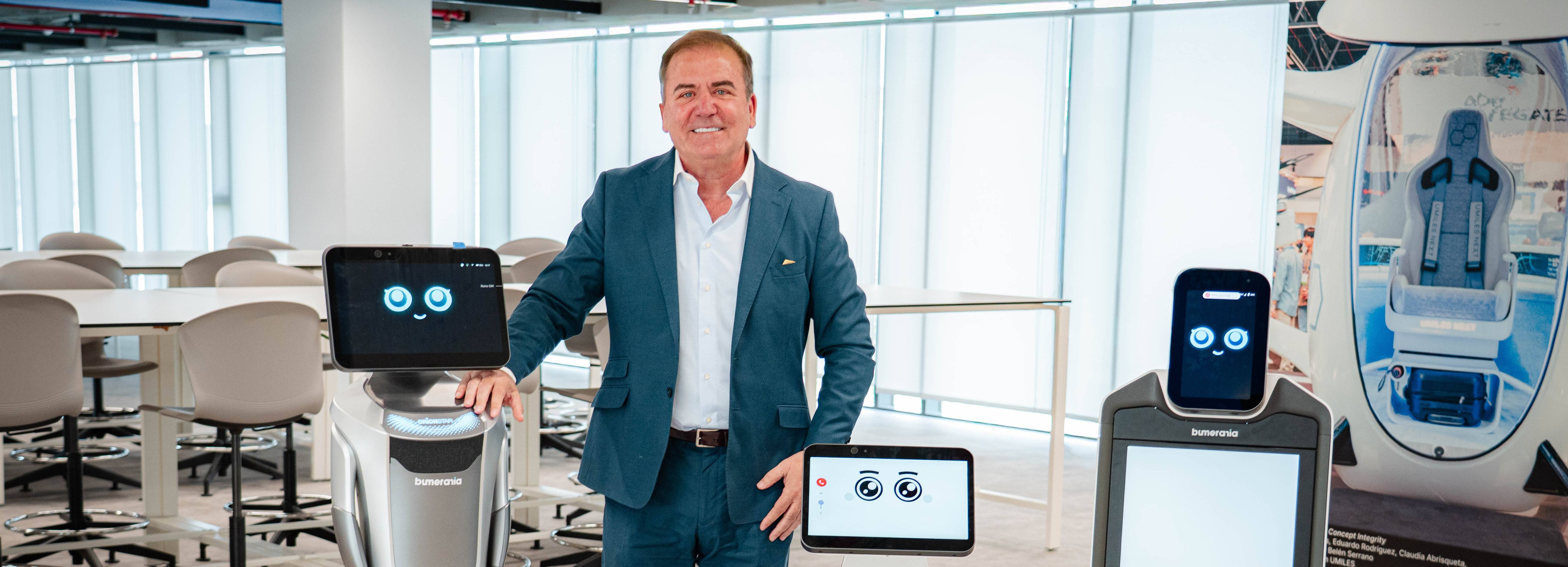 Un hombre sonriente se encuentra junto a varios robots en un ambiente moderno y luminoso.