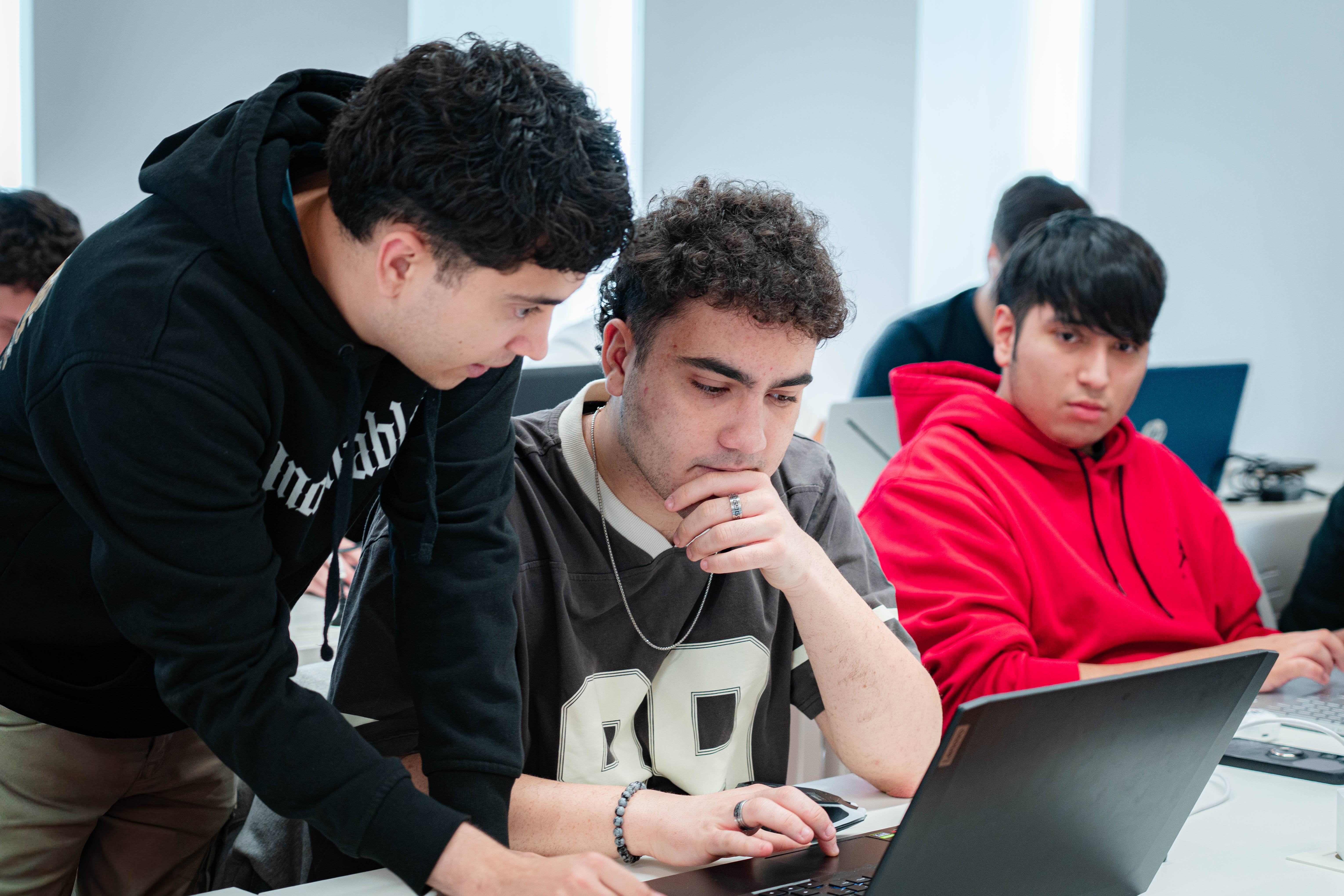 Un grupo de jóvenes se concentra en el trabajo colaborativo frente a una computadora en un aula.