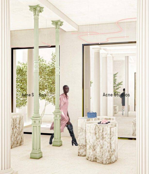 Una tienda de moda contemporánea con columnas verdes, mesas de mármol y un modelo vistiendo un abrigo largo.