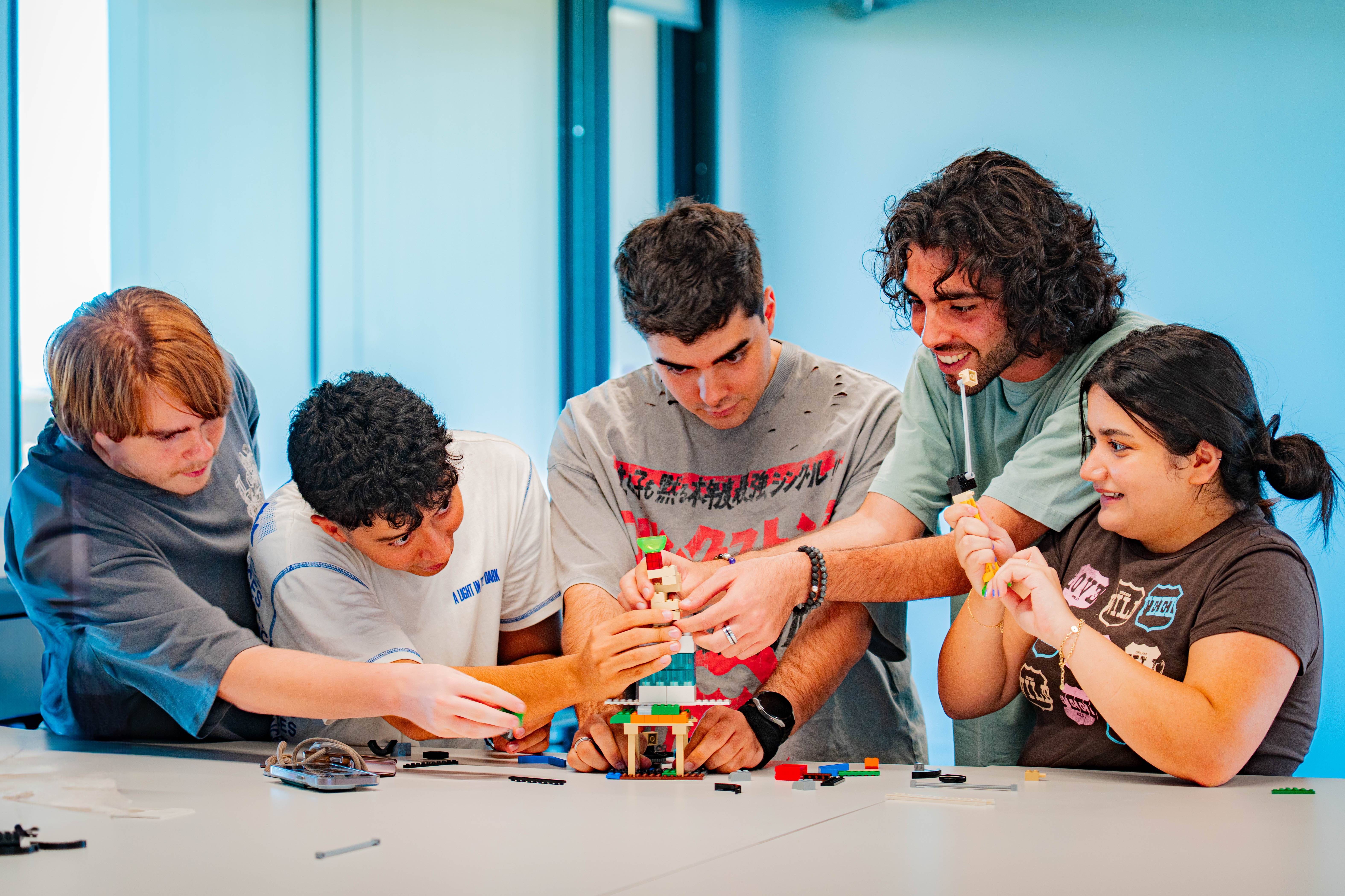 Un grupo de cinco personas colaborando para construir un objeto con bloques de colores en una mesa.