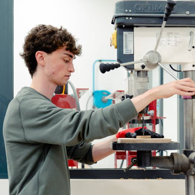 Un joven está utilizando una máquina de taladrar en un taller.