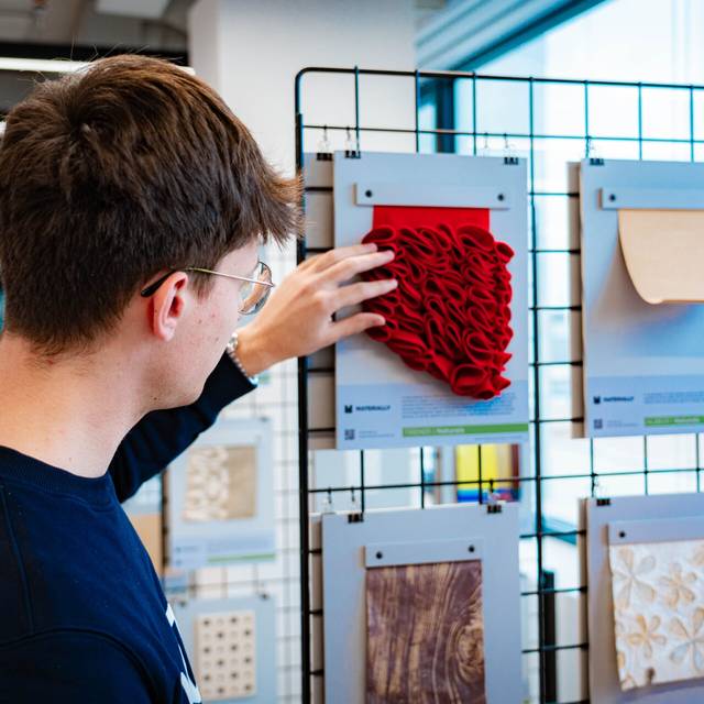 Una persona está tocando un objeto de tela roja expuesto en una pared de exhibición.