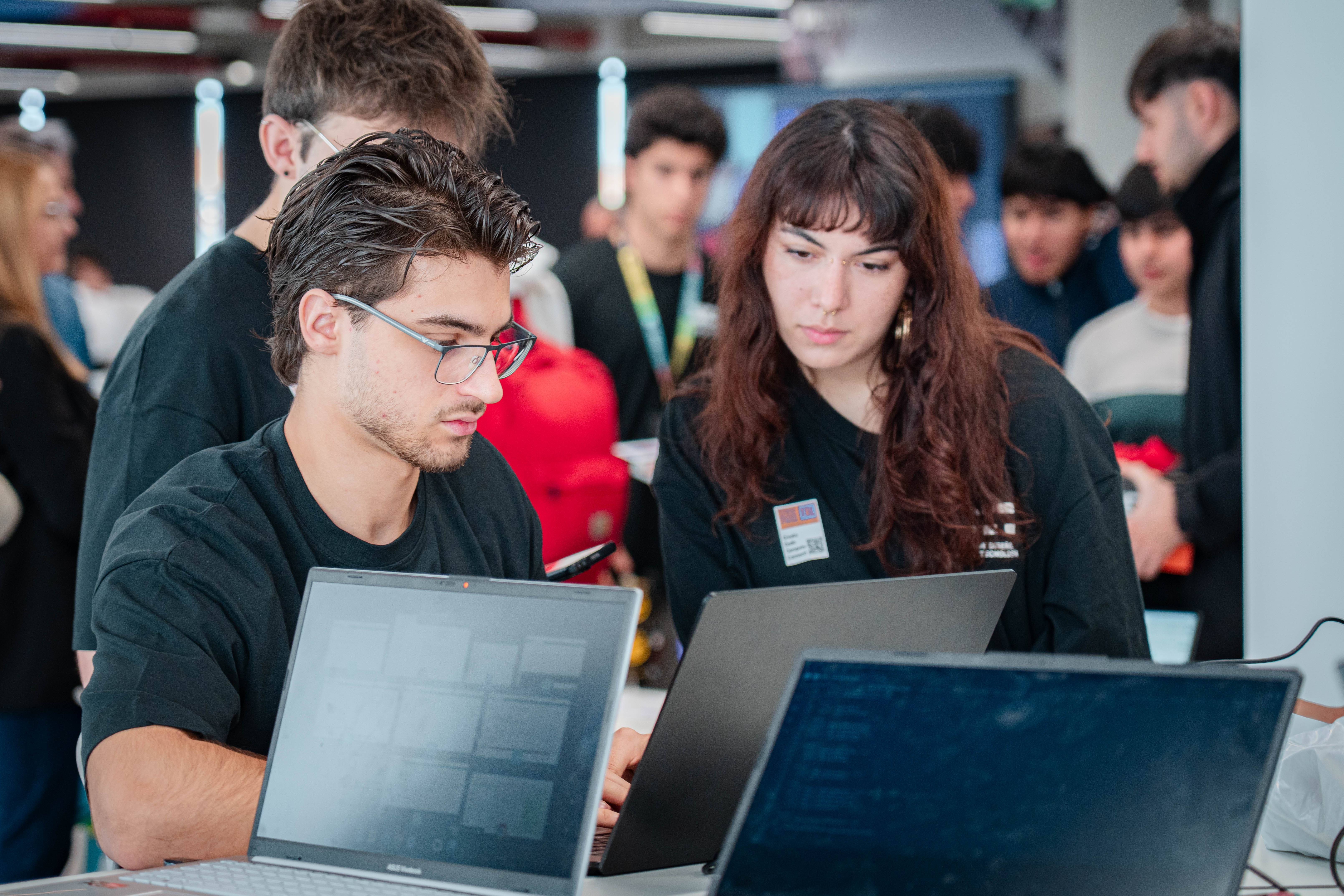 Un grupo de jóvenes interactúa frente a varias pantallas de computadora en un entorno colaborativo.
