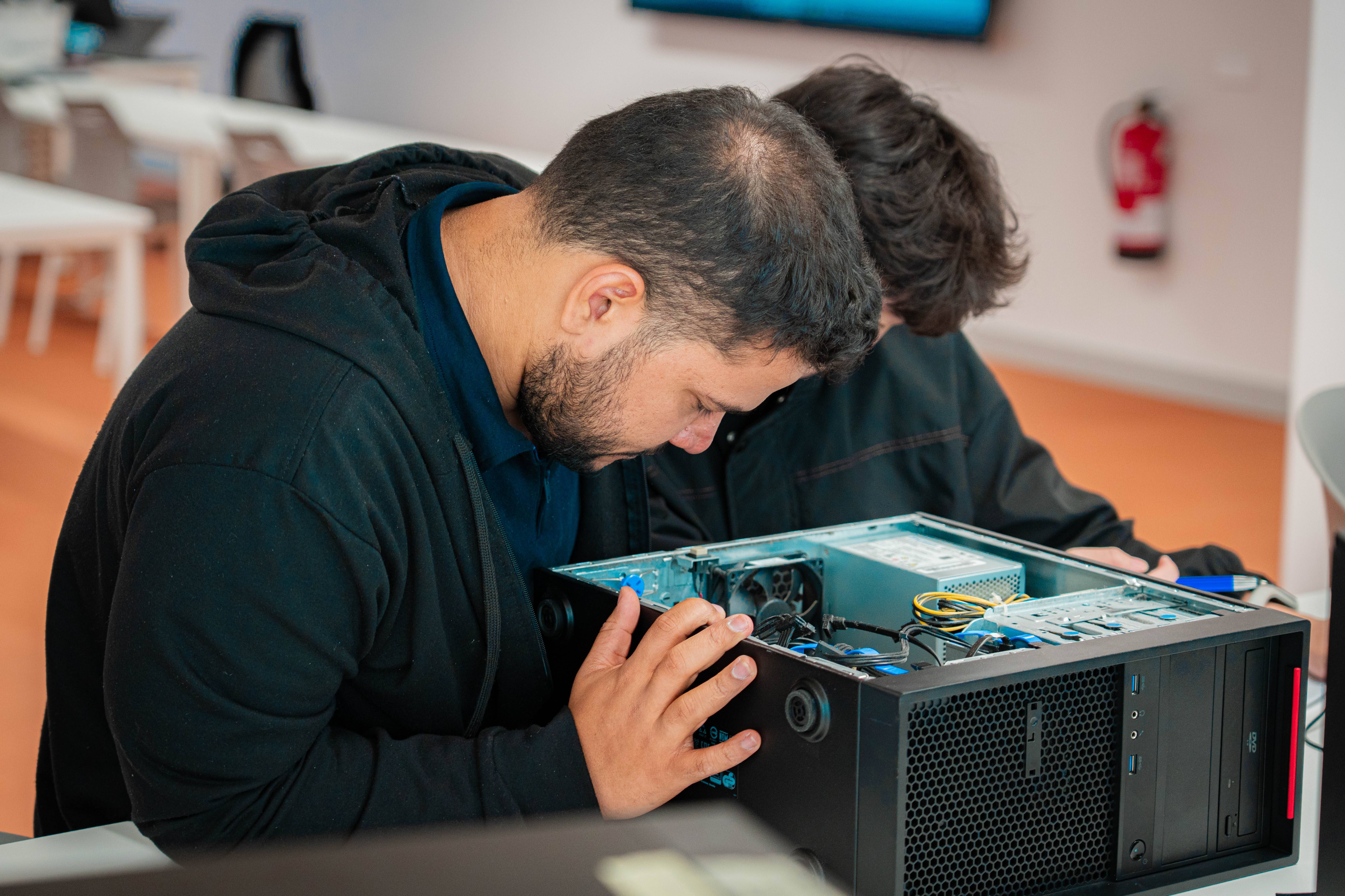Dos personas están trabajando en el interior de una computadora de escritorio.