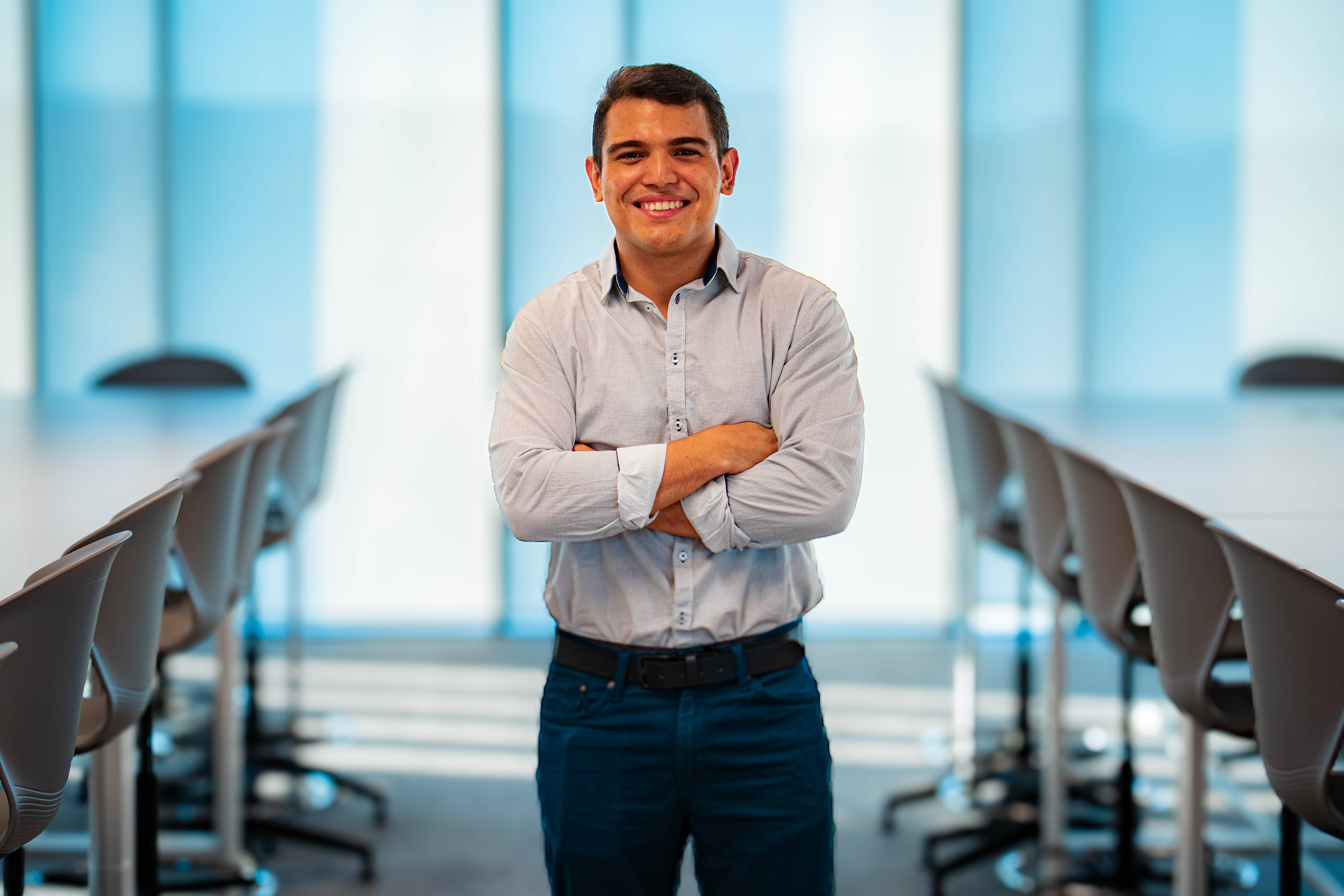 Un joven sonriente se encuentra de pie en una sala de reuniones con paneles de vidrio.
