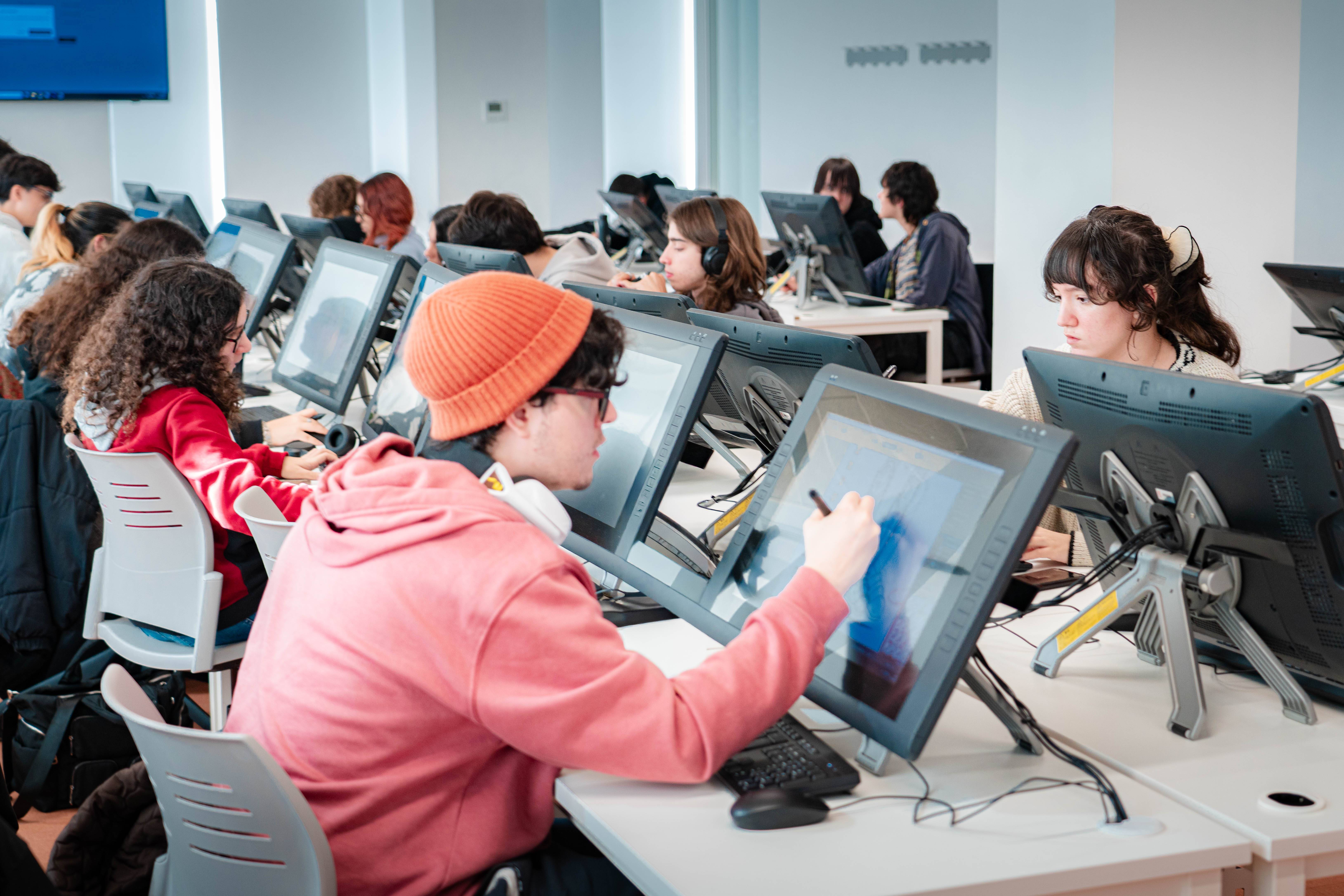 Un grupo de estudiantes trabaja en computadoras con pantallas táctiles en un aula moderna.