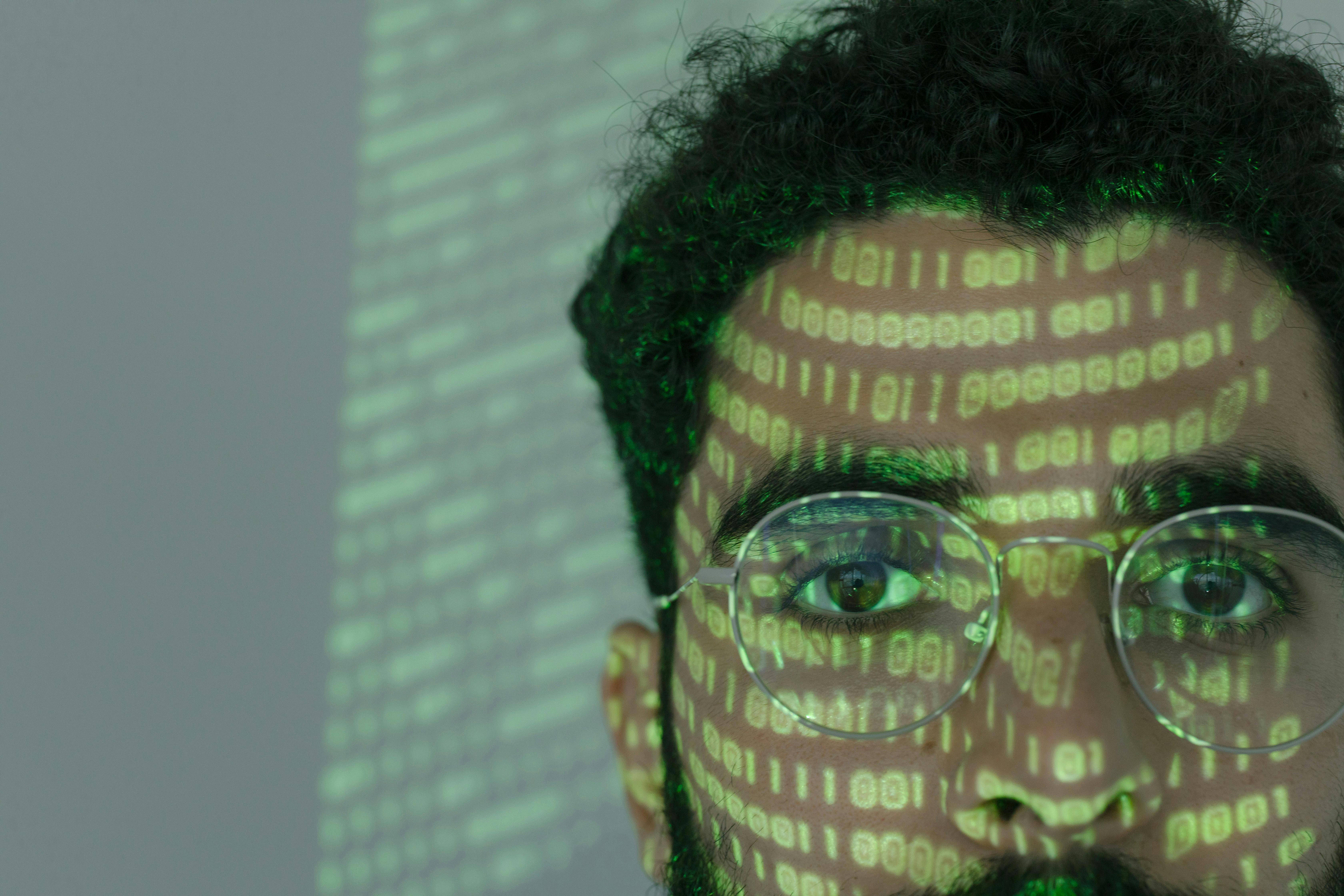 Un hombre con gafas es iluminado por proyecciones de códigos binarios en su rostro.