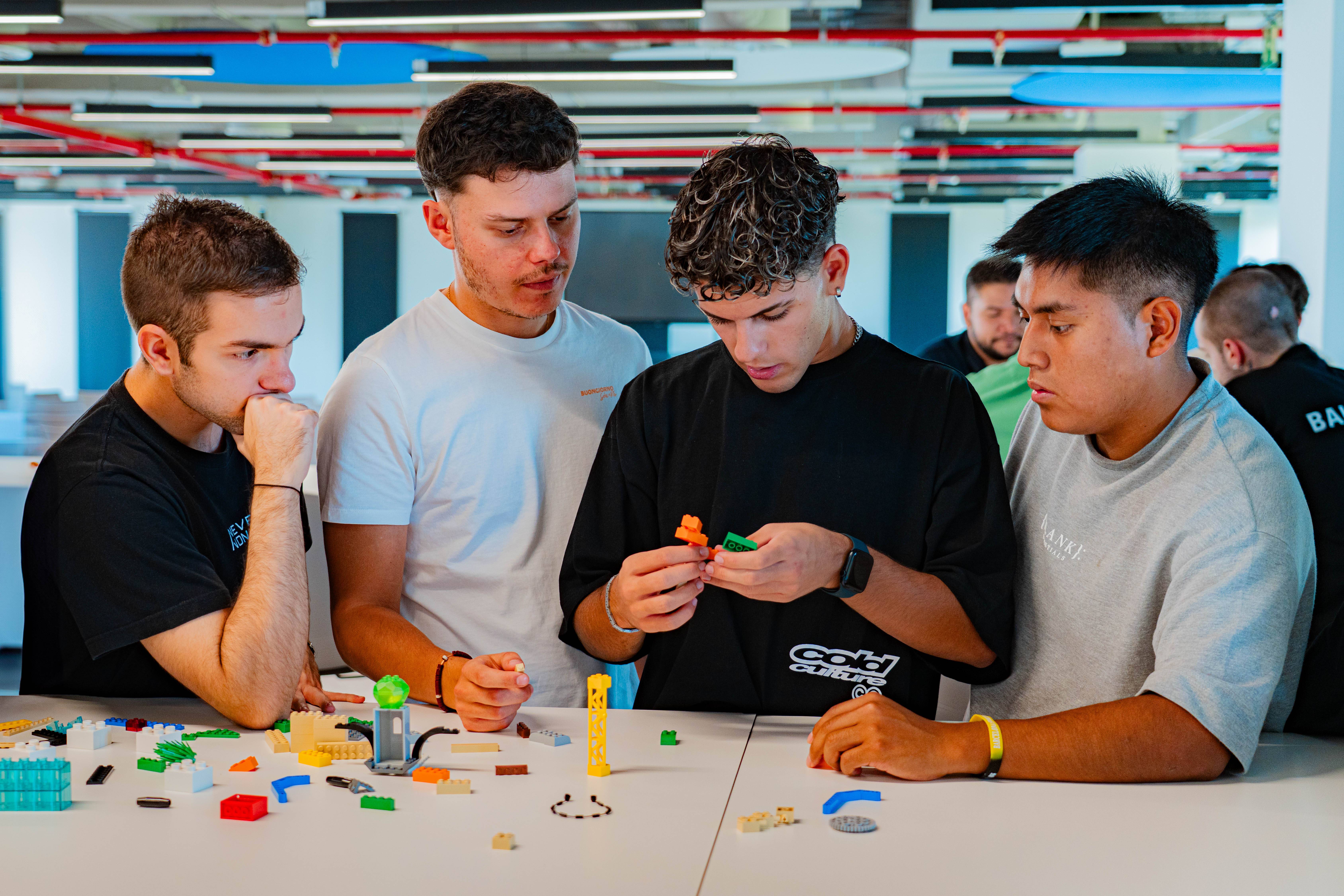 Cuatro jóvenes están colaborando para construir una figura con bloques de plástico en una mesa.