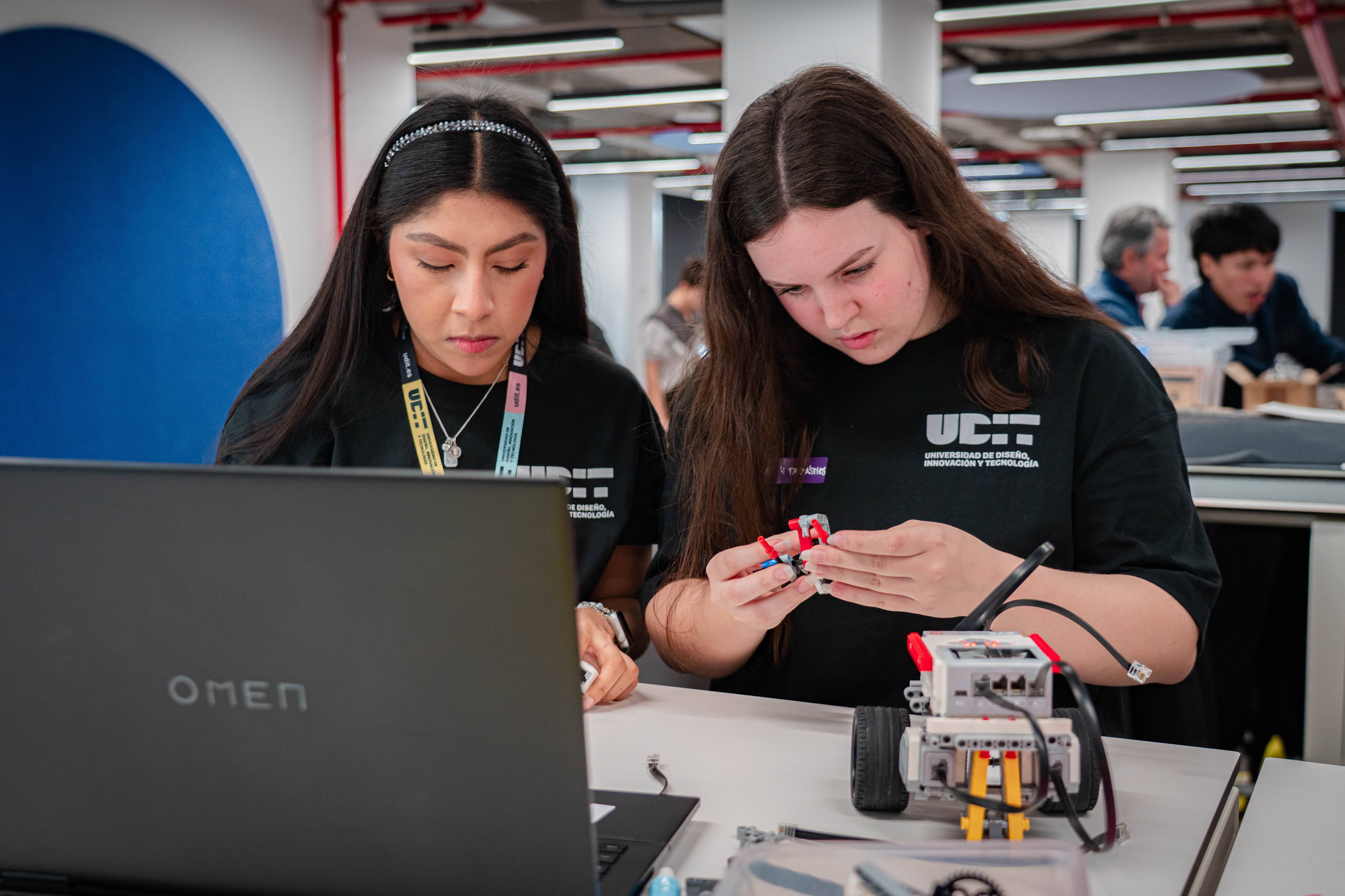 Dos estudiantes trabajan juntas en un proyecto de robótica frente a una computadora portátil.