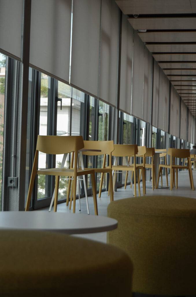 Una vista de un interior con sillas amarillas y mesas redondas en un ambiente moderno y luminoso.