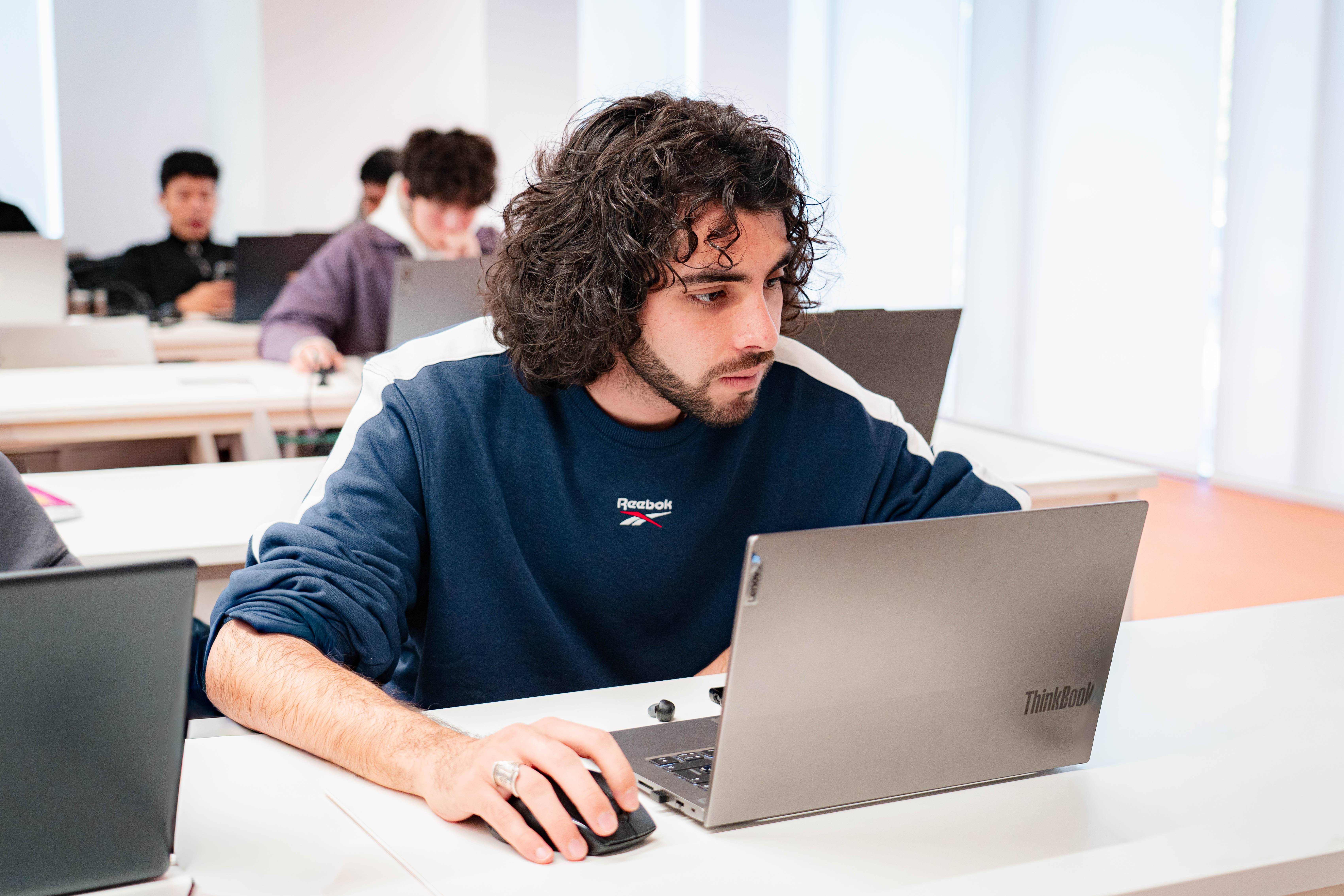 Un estudiante concentrado utilizando una computadora portátil en un aula.