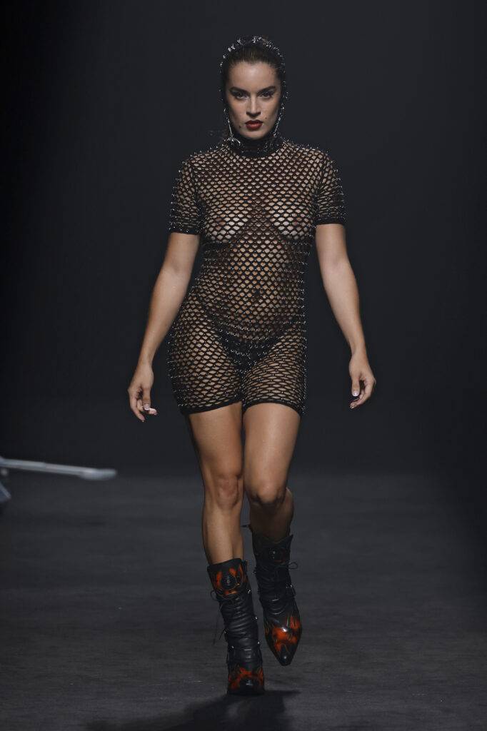 Una modelo camina con un vestido de malla negra en la pasarela.