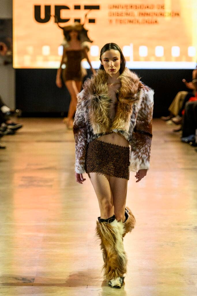 Modelo desfilando con un atuendo elaborado con pieles y materiales brillantes en una pasarela.