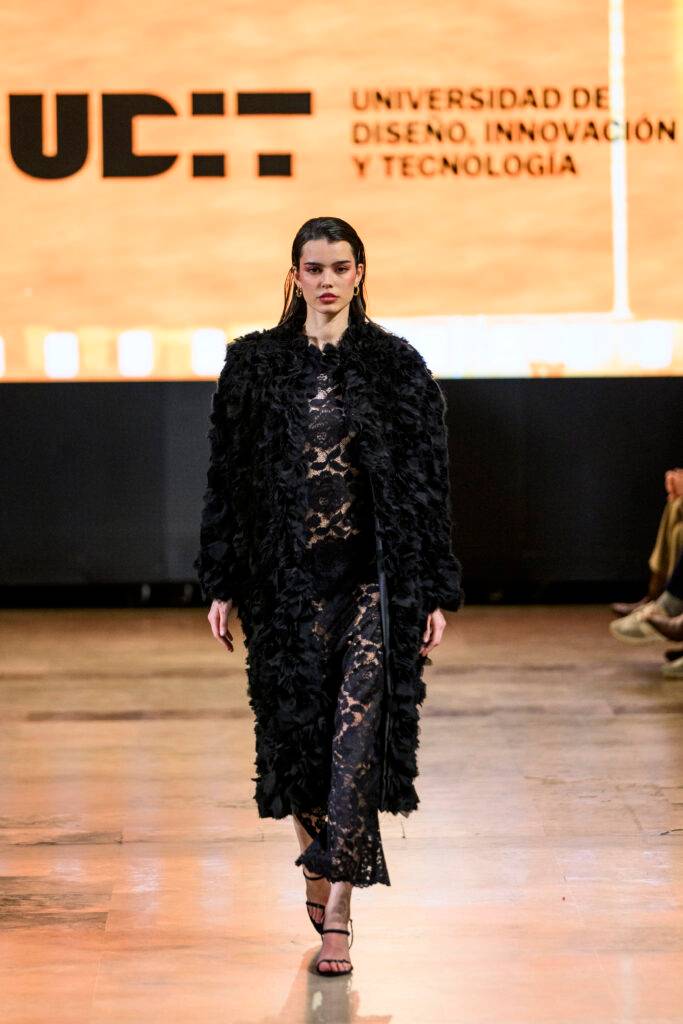 Una modelo desfila con un abrigo negro en un evento de moda en la UDIT.
