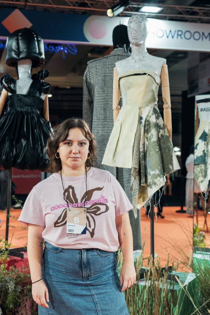 Una persona posa frente a un escaparate de moda con vestidos creativos de fondo.
