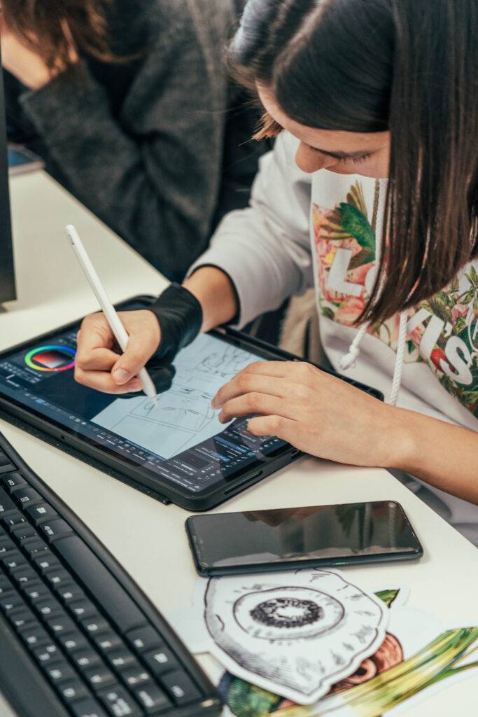 Una persona dibuja en una tablet mientras tiene a su lado un teléfono móvil y un boceto de un ojo.