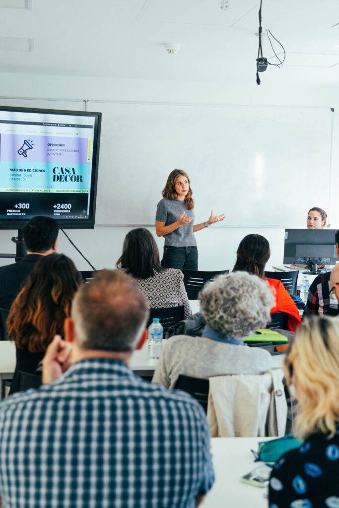 Una mujer presenta información en una sala con un público atento.