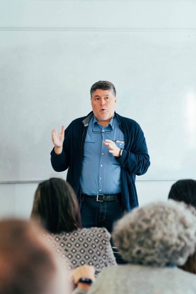 Un hombre está hablando frente a una audiencia en un aula.