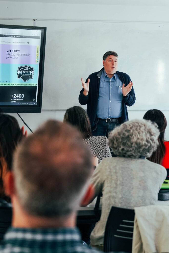 Un profesor está dando una charla frente a un público atento en un aula.