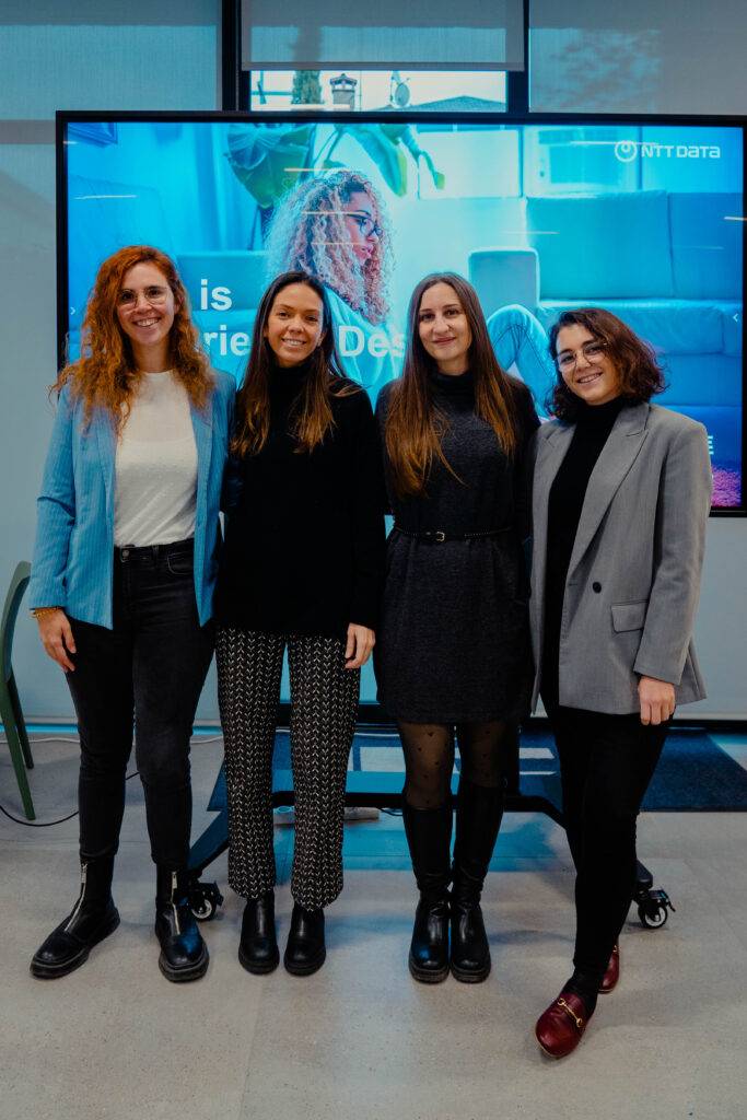 Cuatro mujeres posan sonrientes frente a una pantalla en un evento profesional.