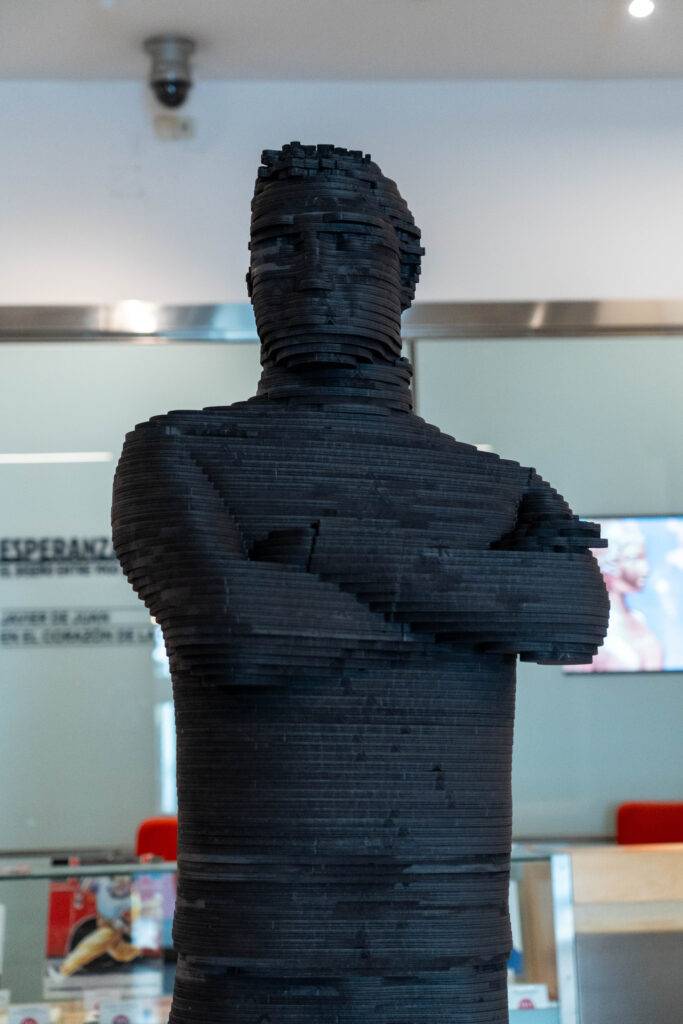 Escultura de un hombre de color negro, compuesta por tiras apiladas horizontalmente.