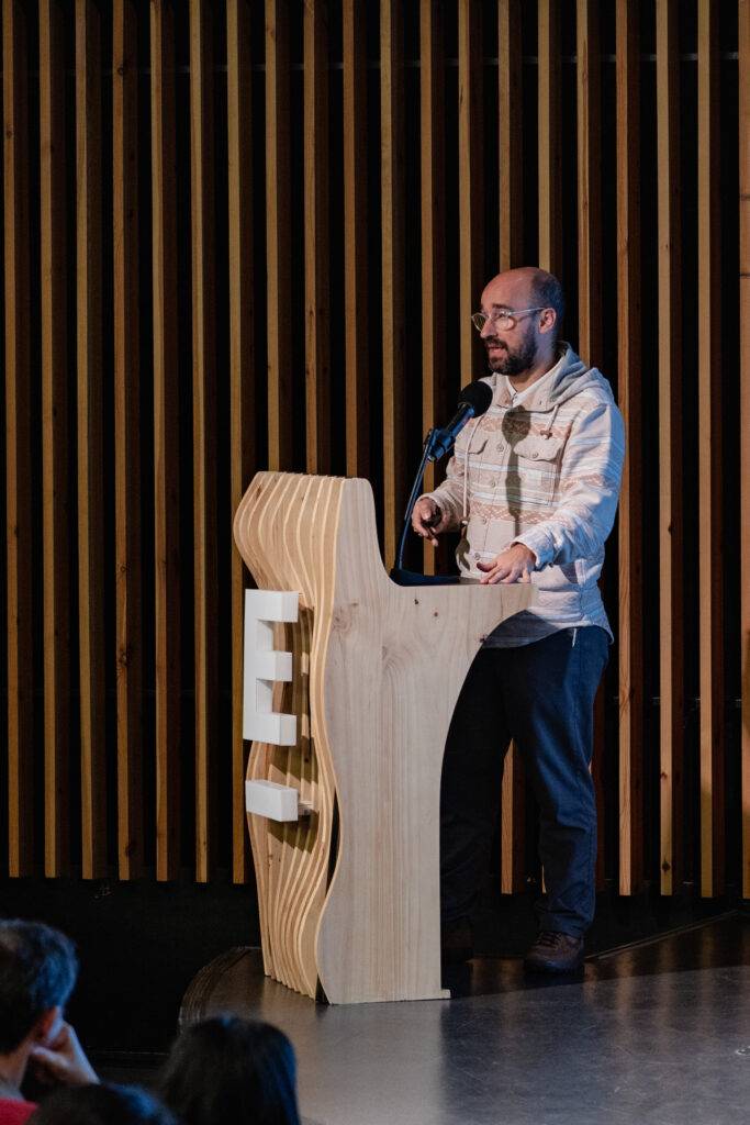 Un hombre habla desde un podio de madera en un evento.