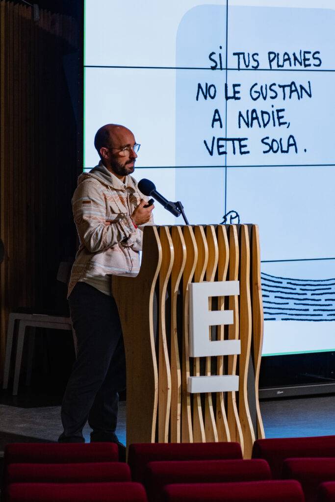 Un hombre pronuncia un discurso frente a un micrófono, mientras se proyecta una frase en una pantalla de fondo.