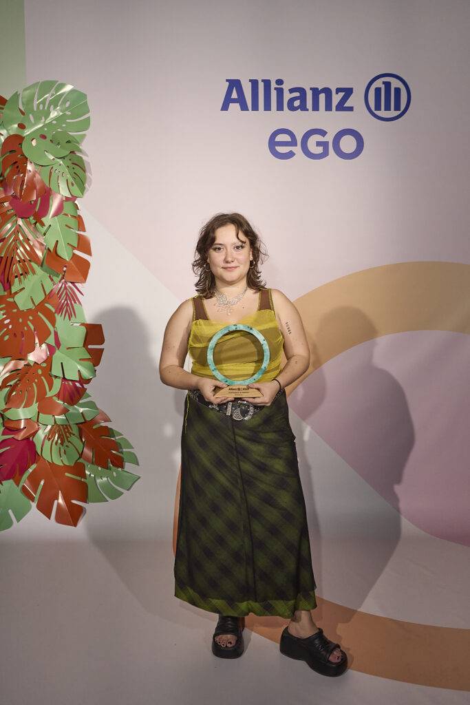 Una persona sostiene un trofeo en un evento, con un fondo decorado y un logo visible de Allianz.