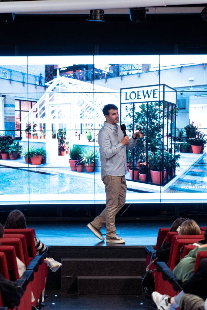 Un hombre habla en el escenario frente a una gran pantalla que muestra un espacio con plantas y el nombre de la marca Loewe.